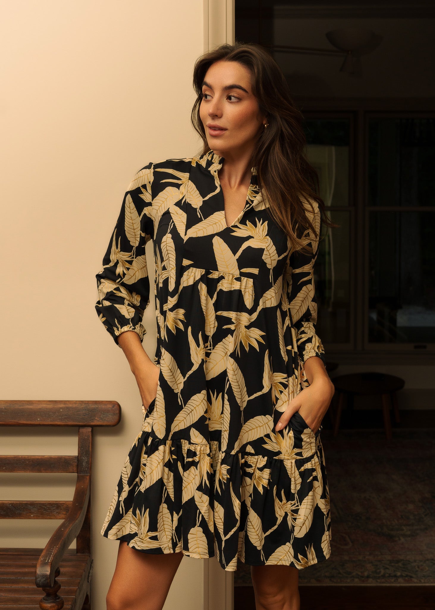 Woman wearing a black and gold patterned dress standing indoors.