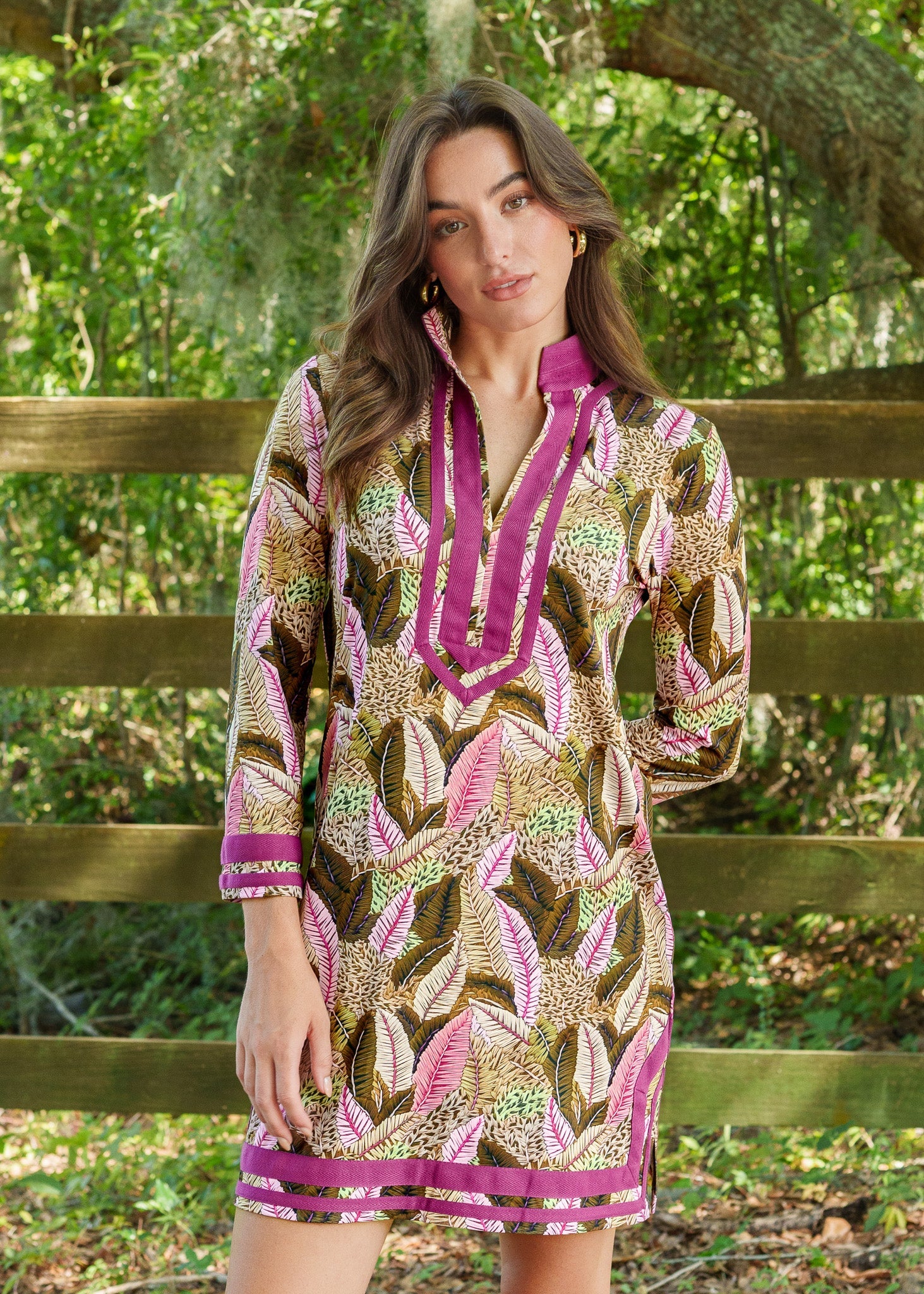 Woman wearing a patterned dress with a pink collar and cuffs, standing outdoors with greenery in the background.