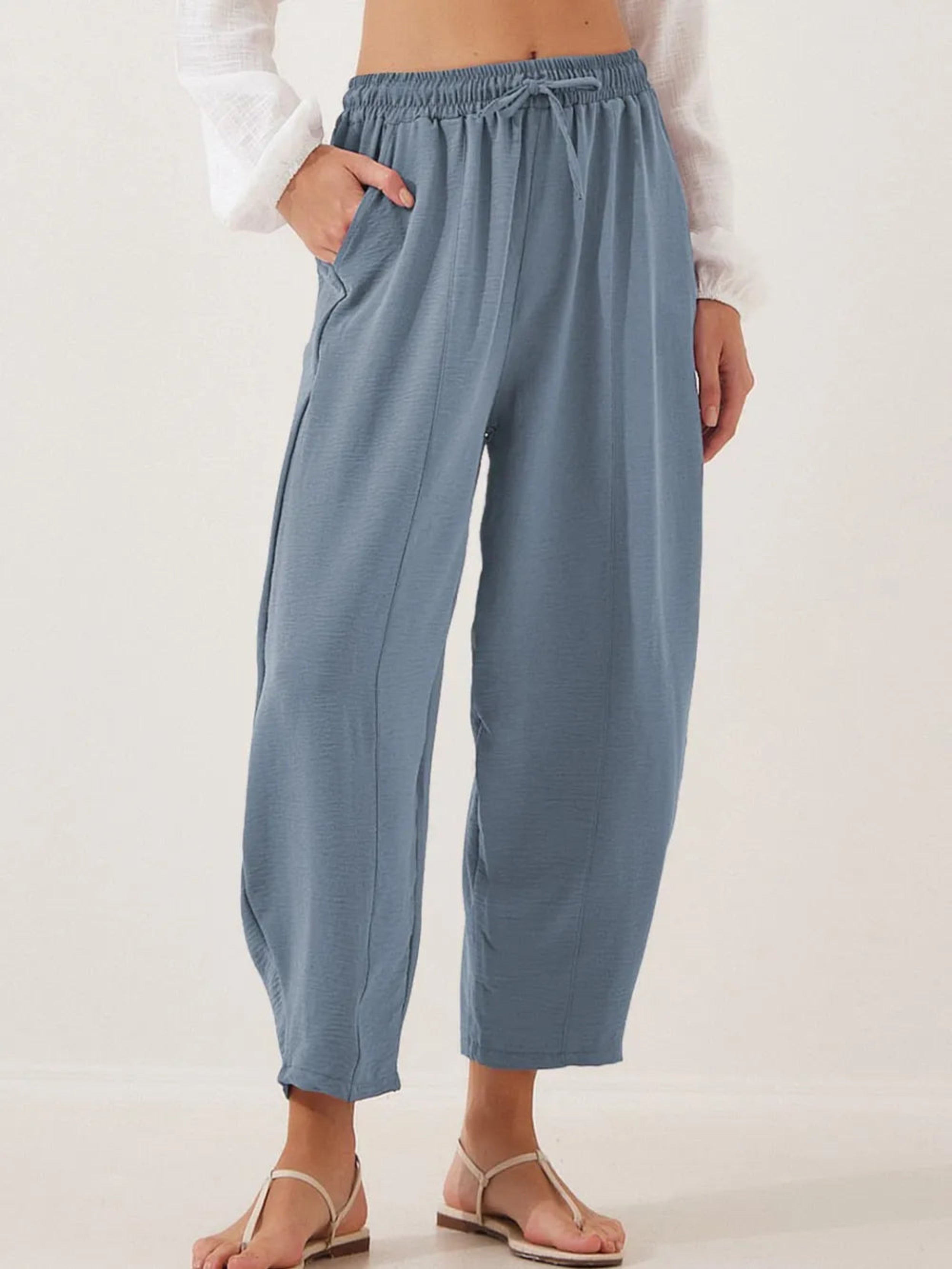 A pair of blue cropped jogger pants with a drawstring waist, displayed on a model without showing the upper part of the body.