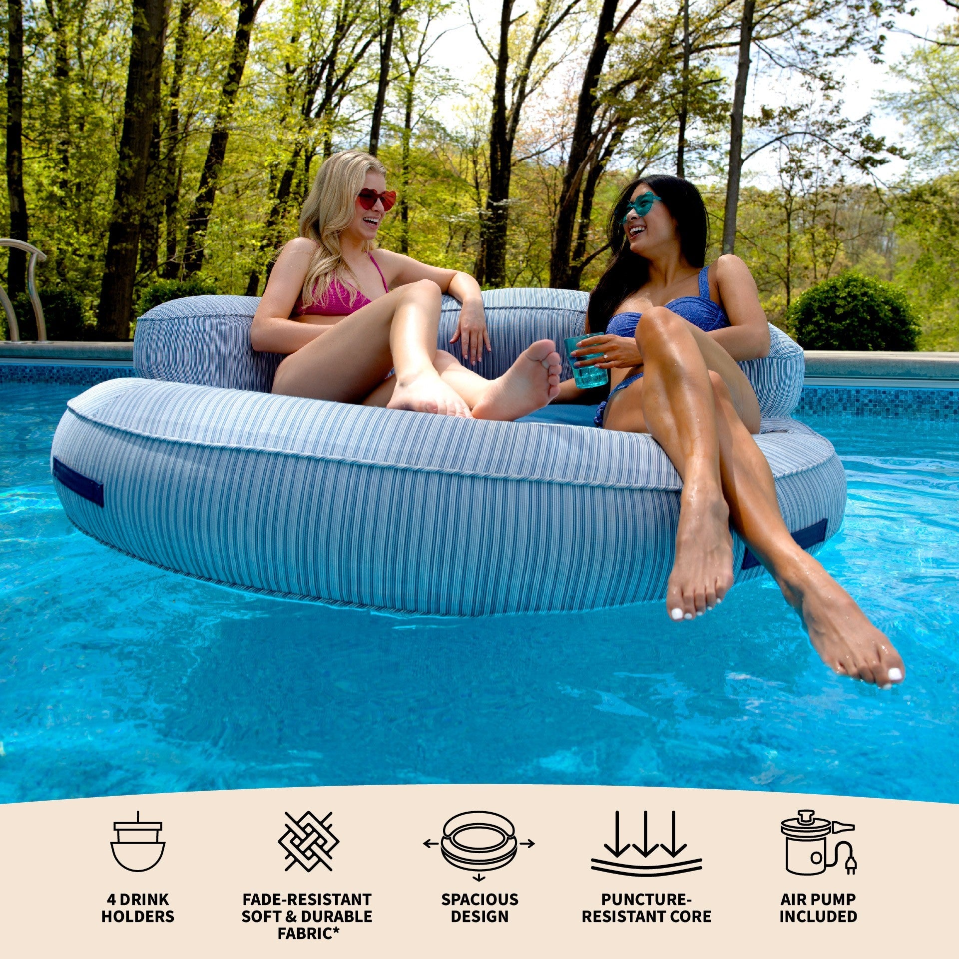 Two women lounging on a inflatable pool float in a pool with surrounding trees.