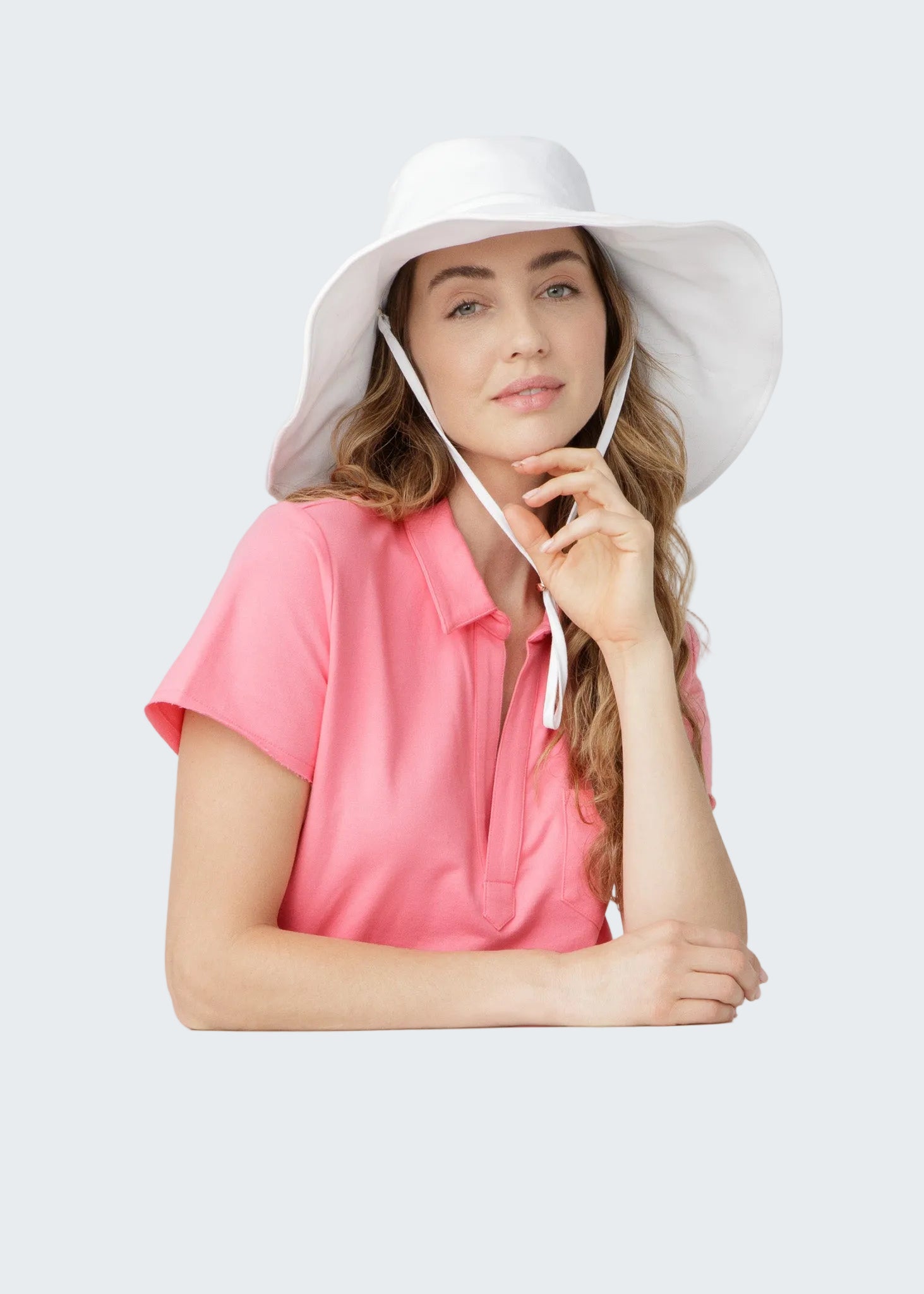 Woman wearing a white sun hat and pink shirt on a light gray background