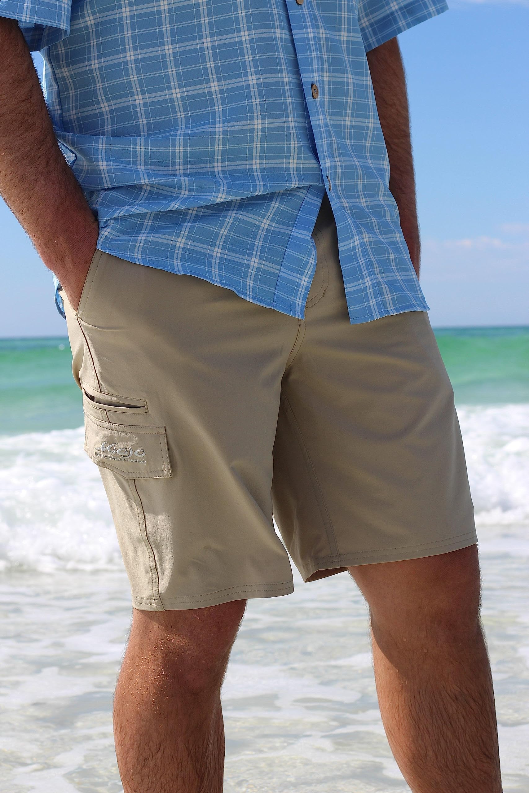 Person wearing a blue plaid shirt and beige shorts standing on a beach.