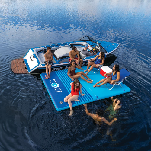 Group of people on a blue inflatable platform in the water with a boat nearby.
