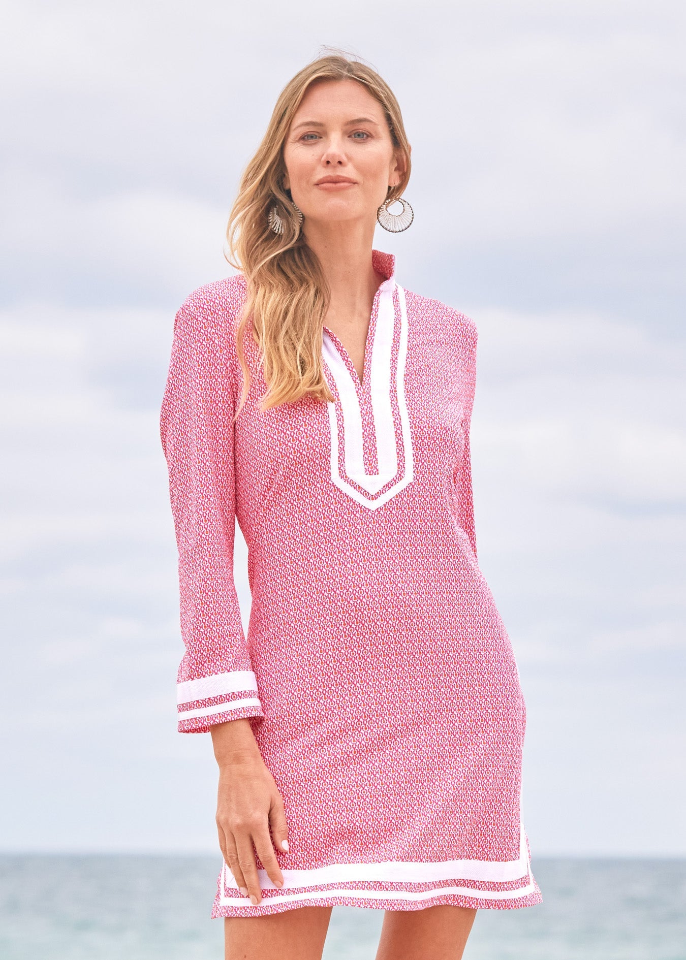 Woman wearing a pink dress with white trim against a light blue sky.