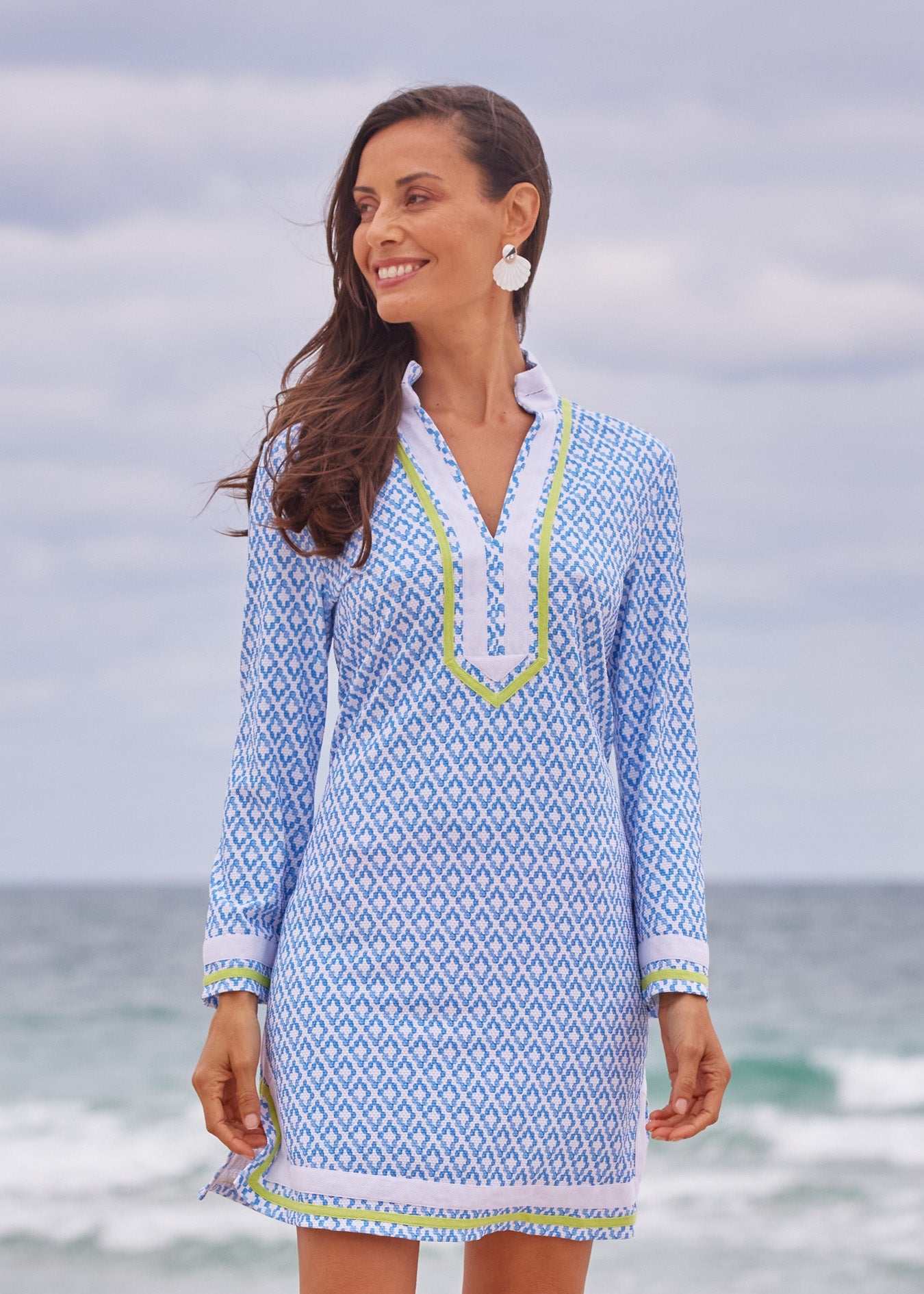 Woman wearing a blue patterned dress with a white collar on a beach.