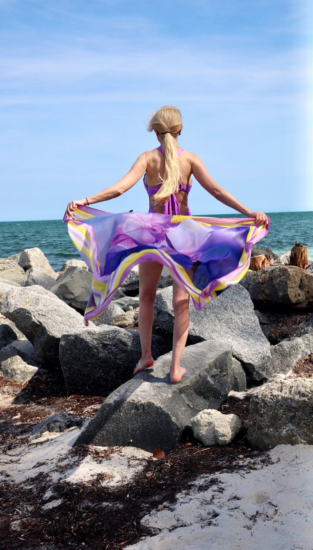 Woman standing on rocks by the sea with a colorful scarf