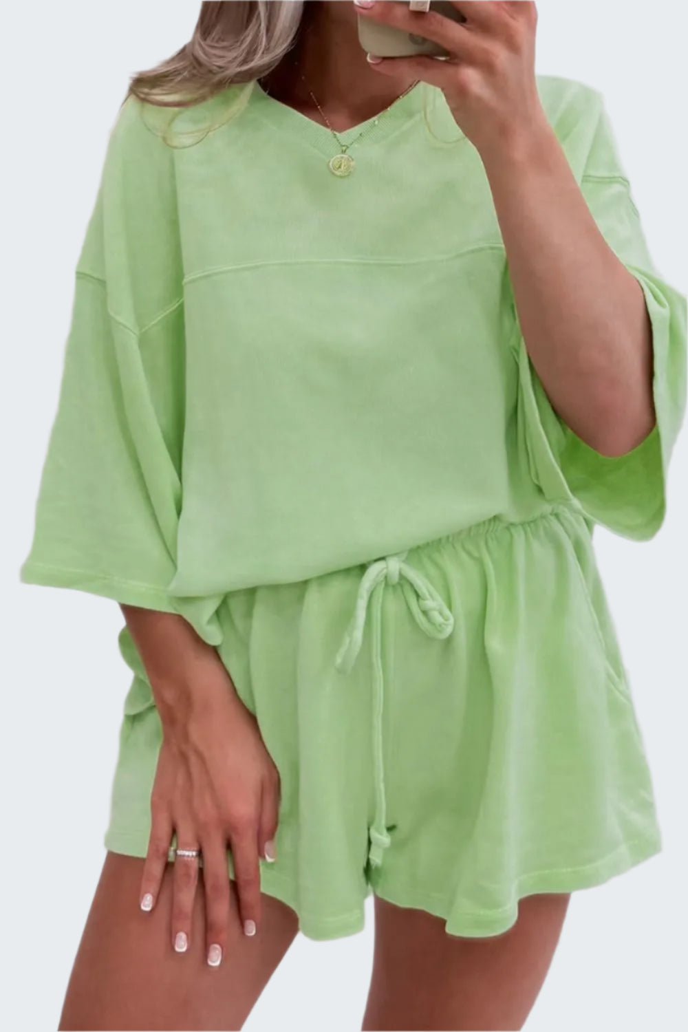A woman wearing a green loose V neck half sleeve tee and matching drawstring shorts, both made of slightly stretchy fabric.