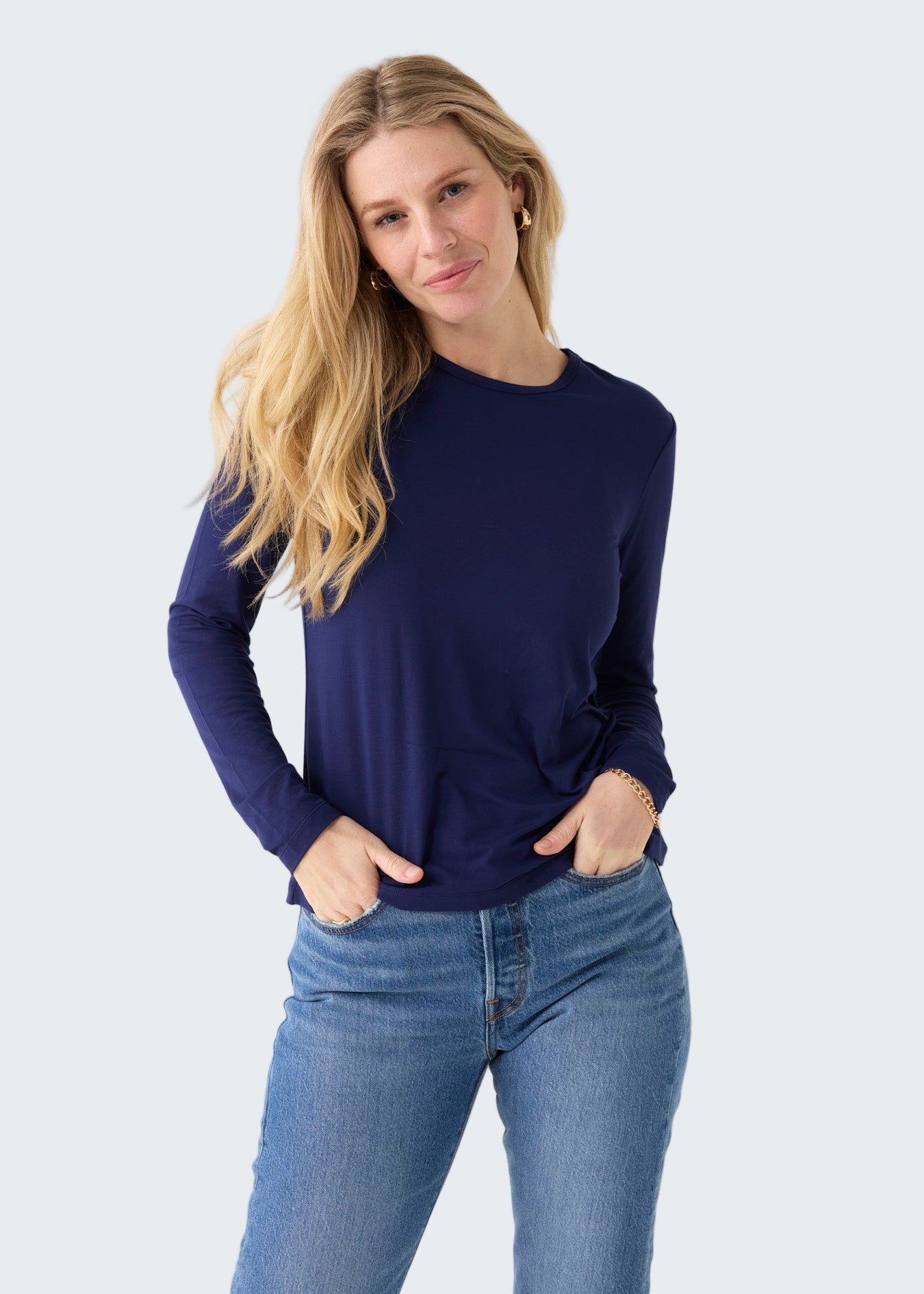 Woman wearing a navy long-sleeve top and blue jeans on a white background