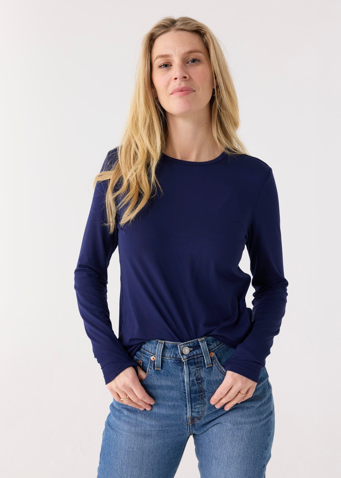 Woman wearing a navy long-sleeve top and blue jeans on a white background