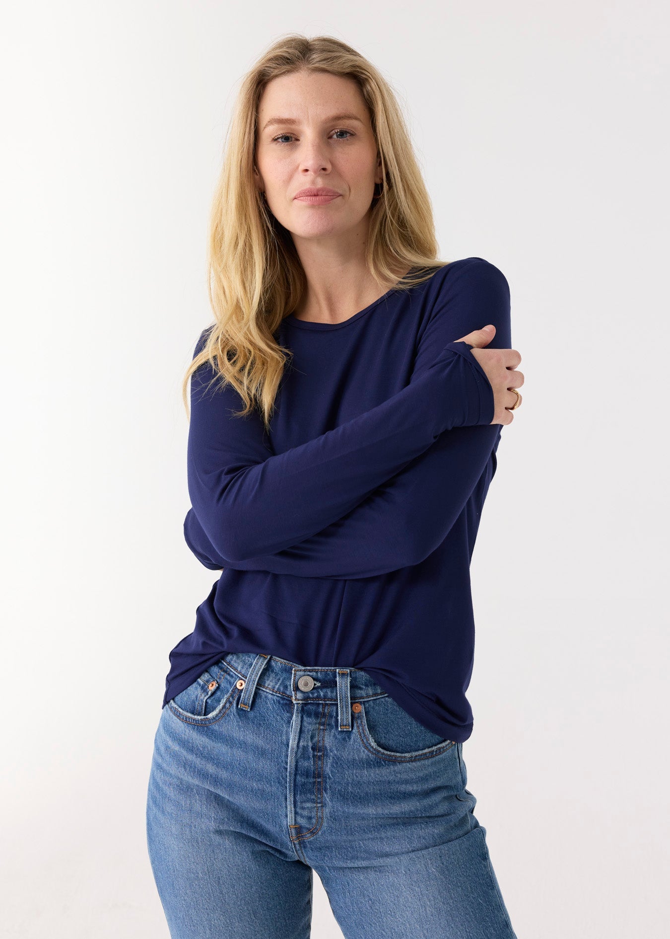 Woman wearing a navy blue long-sleeve top and blue jeans against a white background