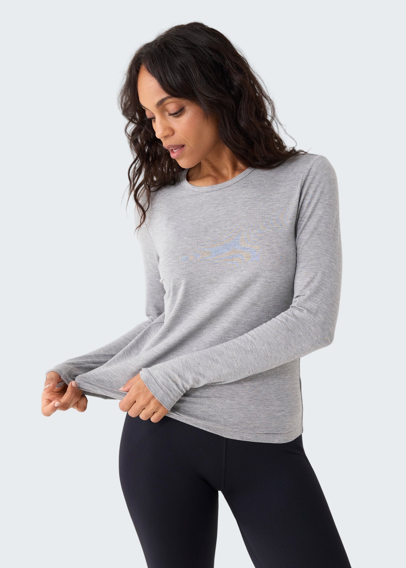 Woman wearing a gray long-sleeve shirt and black leggings on a white background