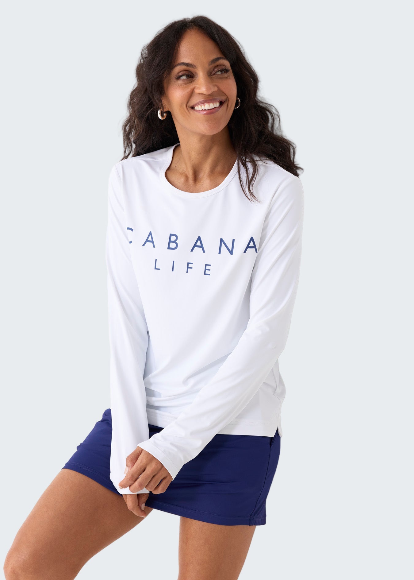 Woman wearing a white long-sleeve shirt with 'CABANA LIFE' text and blue shorts against a white background