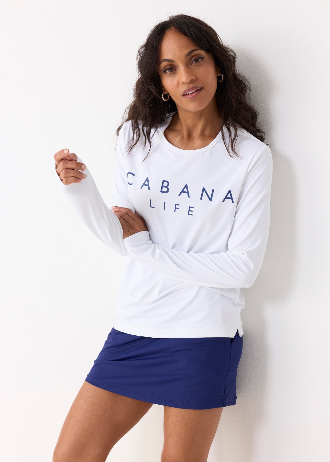 Woman wearing a white 'Cabana Life' long-sleeve shirt and blue skirt against a white background