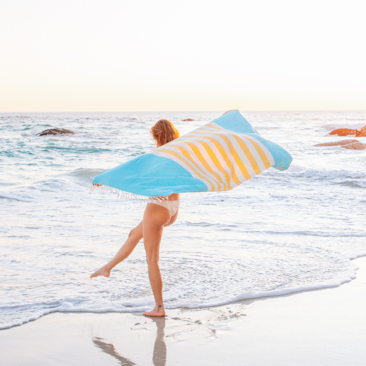 Woman holding a blue and yellow striped towel on a beach