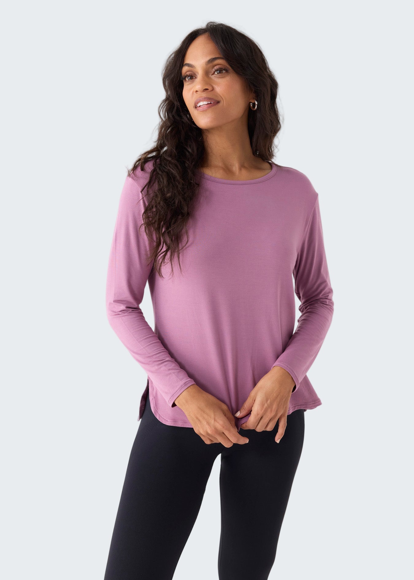 Woman wearing a pink long-sleeve top and black leggings on a white background