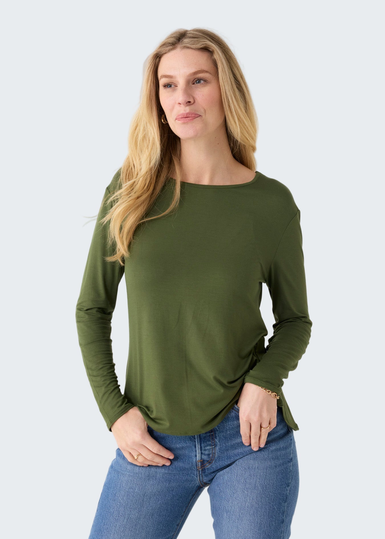 Woman wearing an olive green long-sleeve top and blue jeans on a white background