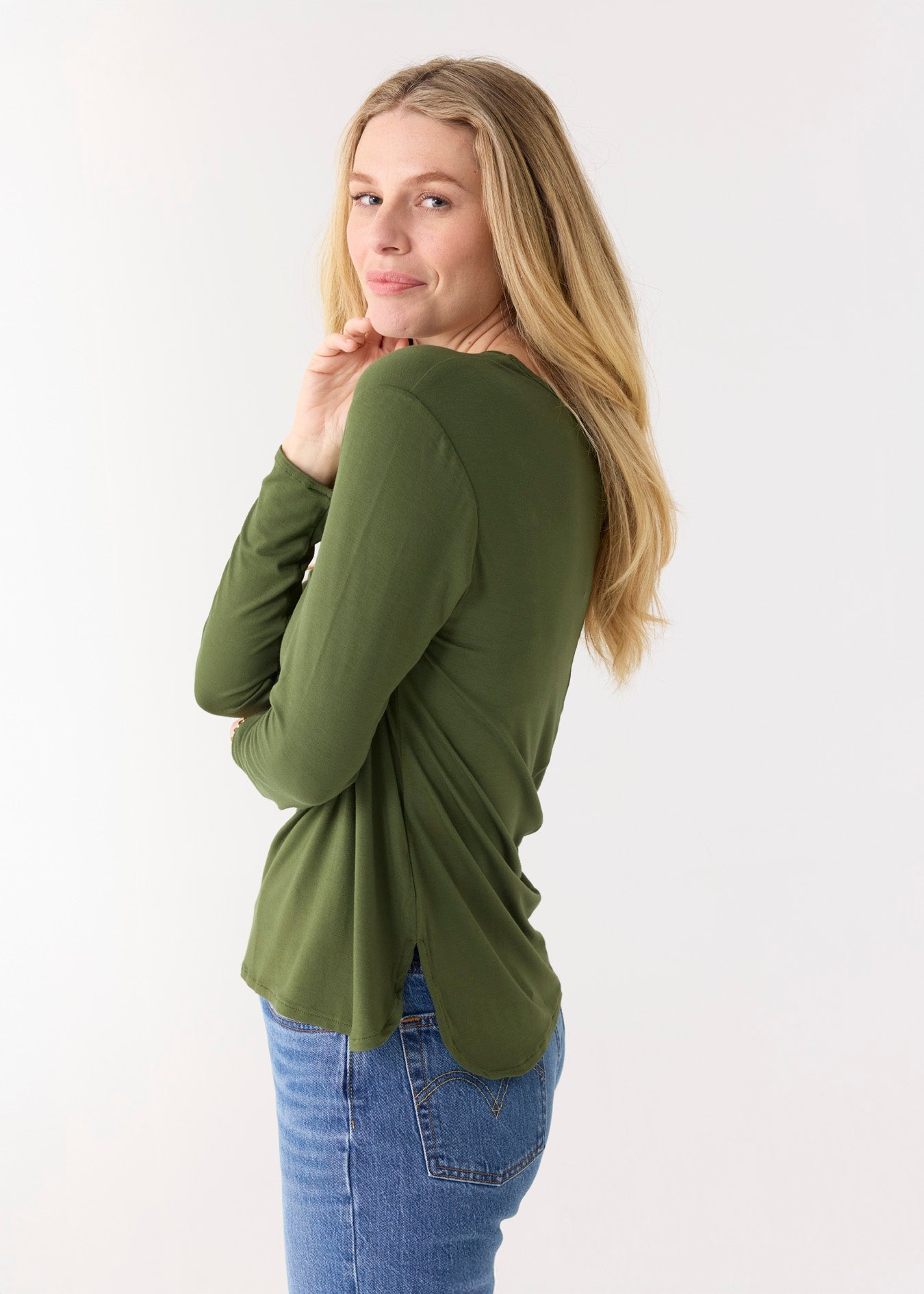 Woman wearing a green long-sleeve top and blue jeans on a white background