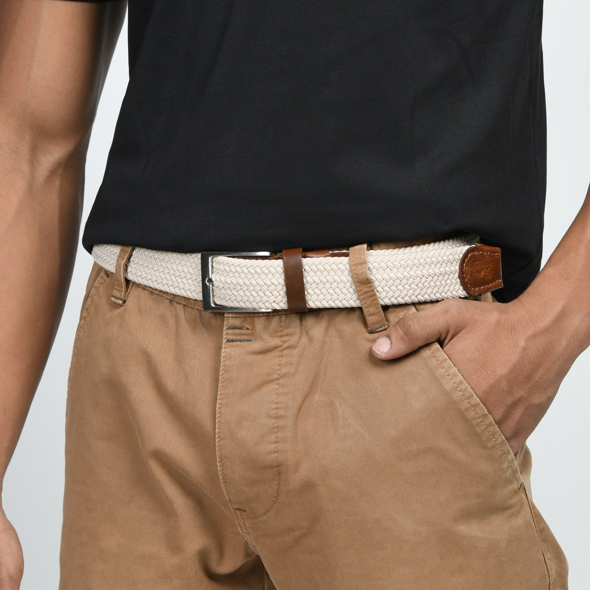 Person wearing a black shirt, beige pants, and a white belt with brown leather buckle on a light gray background