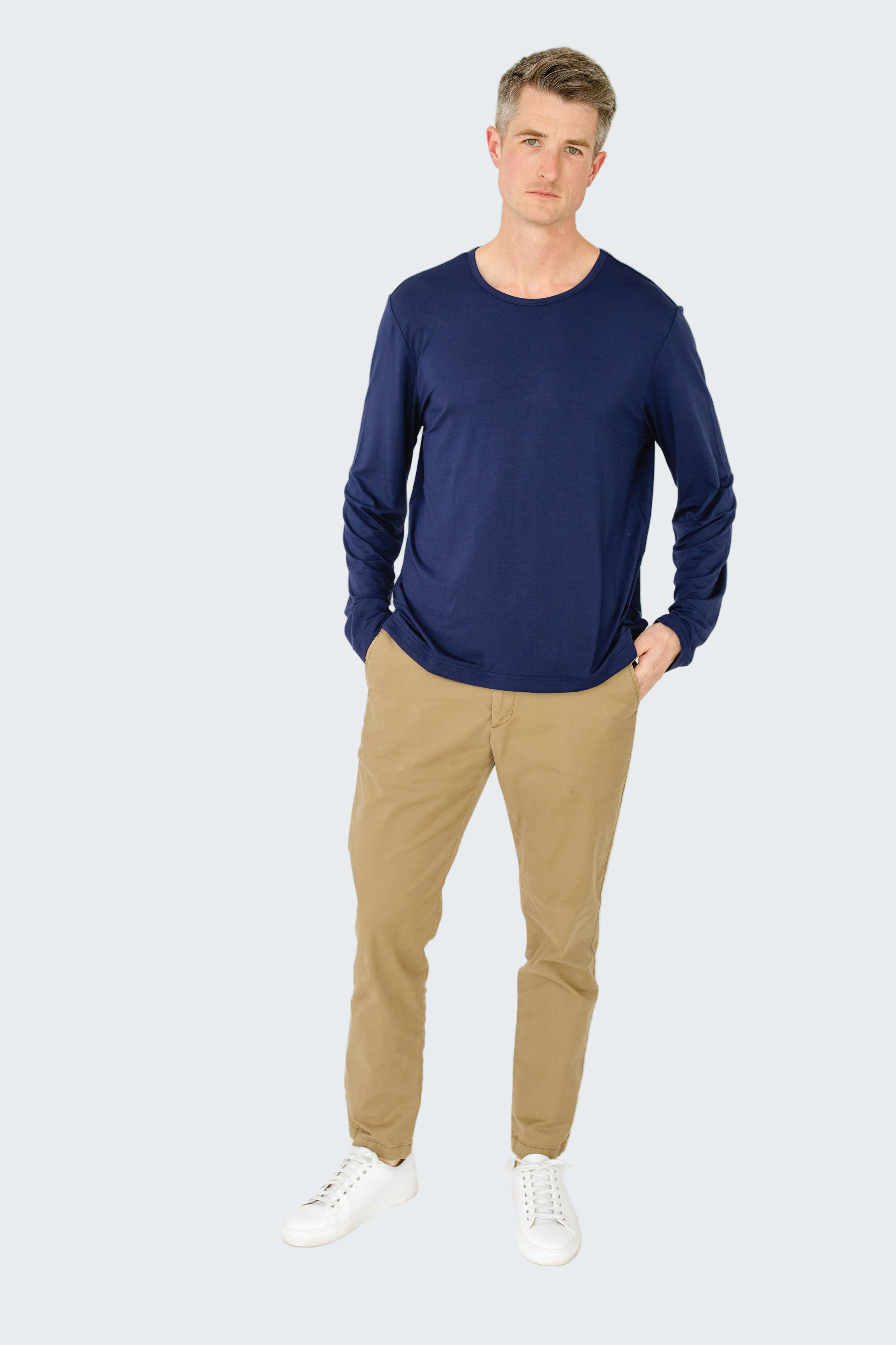 Man wearing a blue long-sleeve shirt and beige pants on a white background