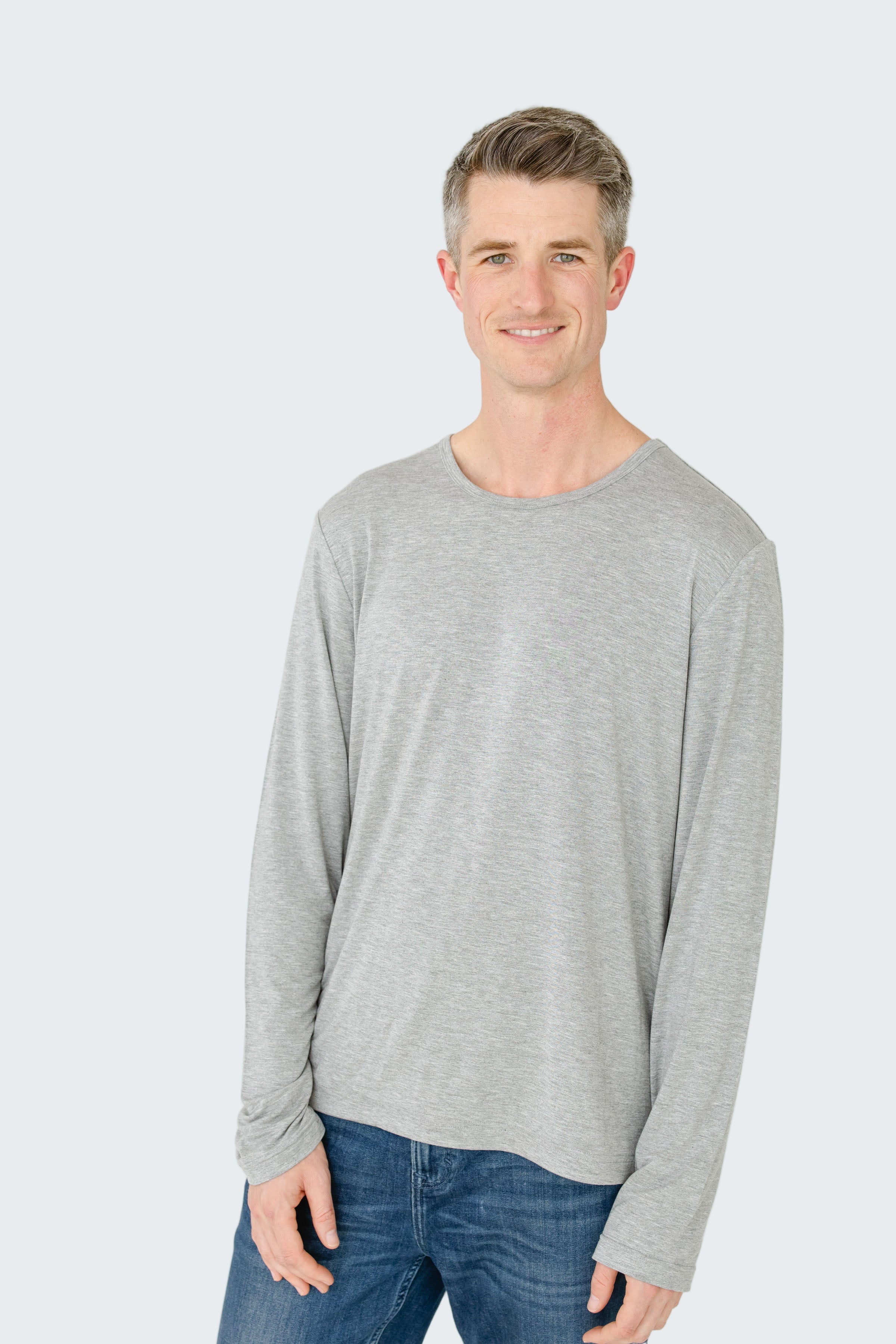 Man wearing a gray long-sleeve shirt and blue jeans on a white background