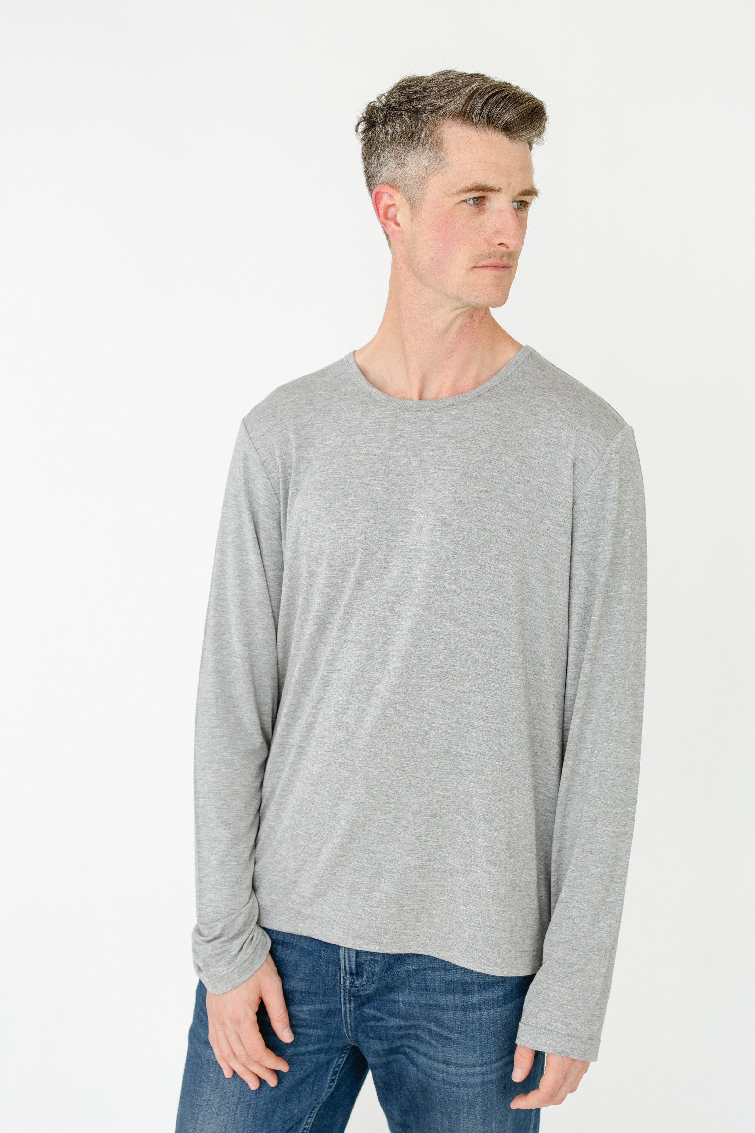 Man wearing a gray long-sleeve shirt and blue jeans on a white background