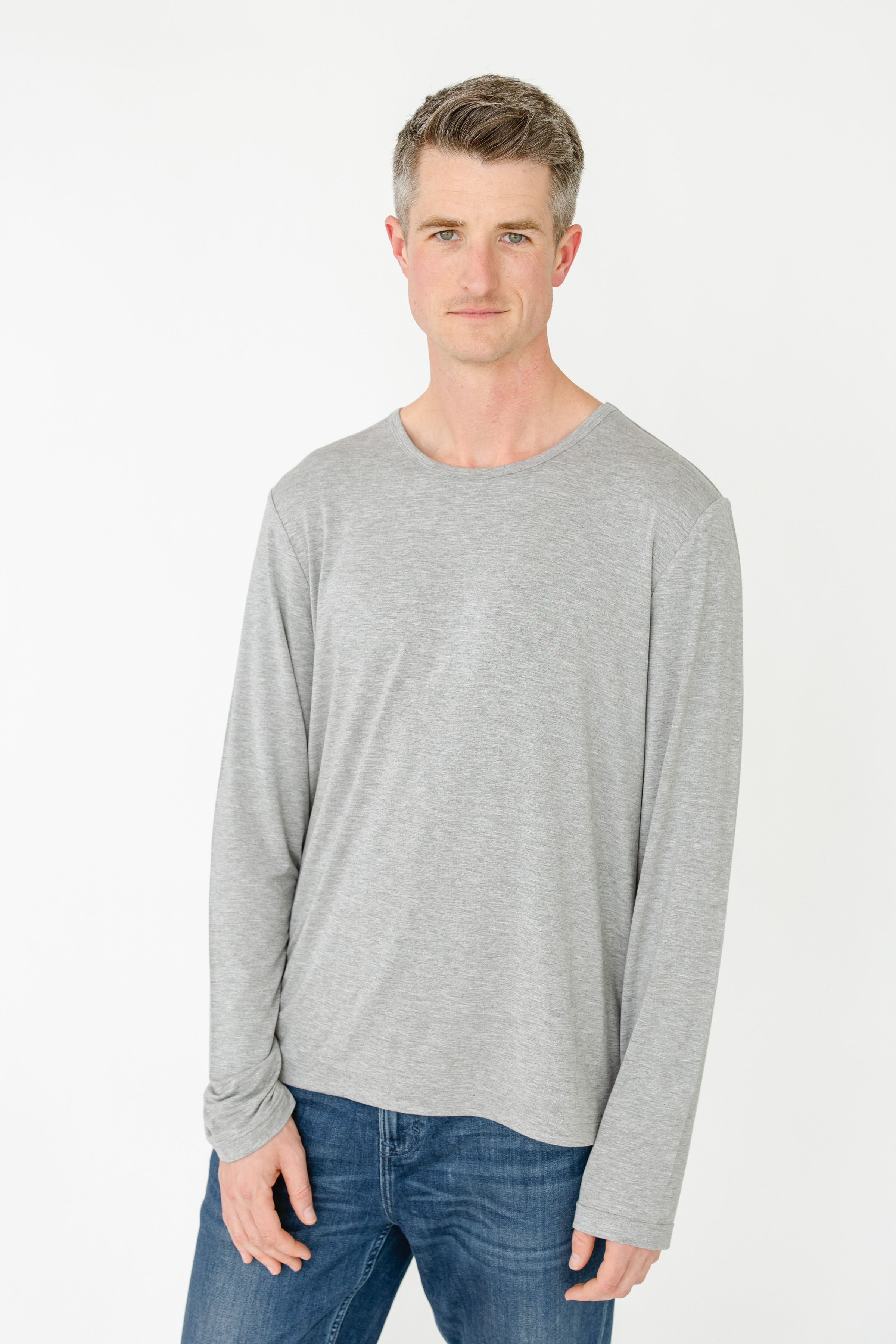 Man wearing a gray long-sleeve shirt and blue jeans on a white background