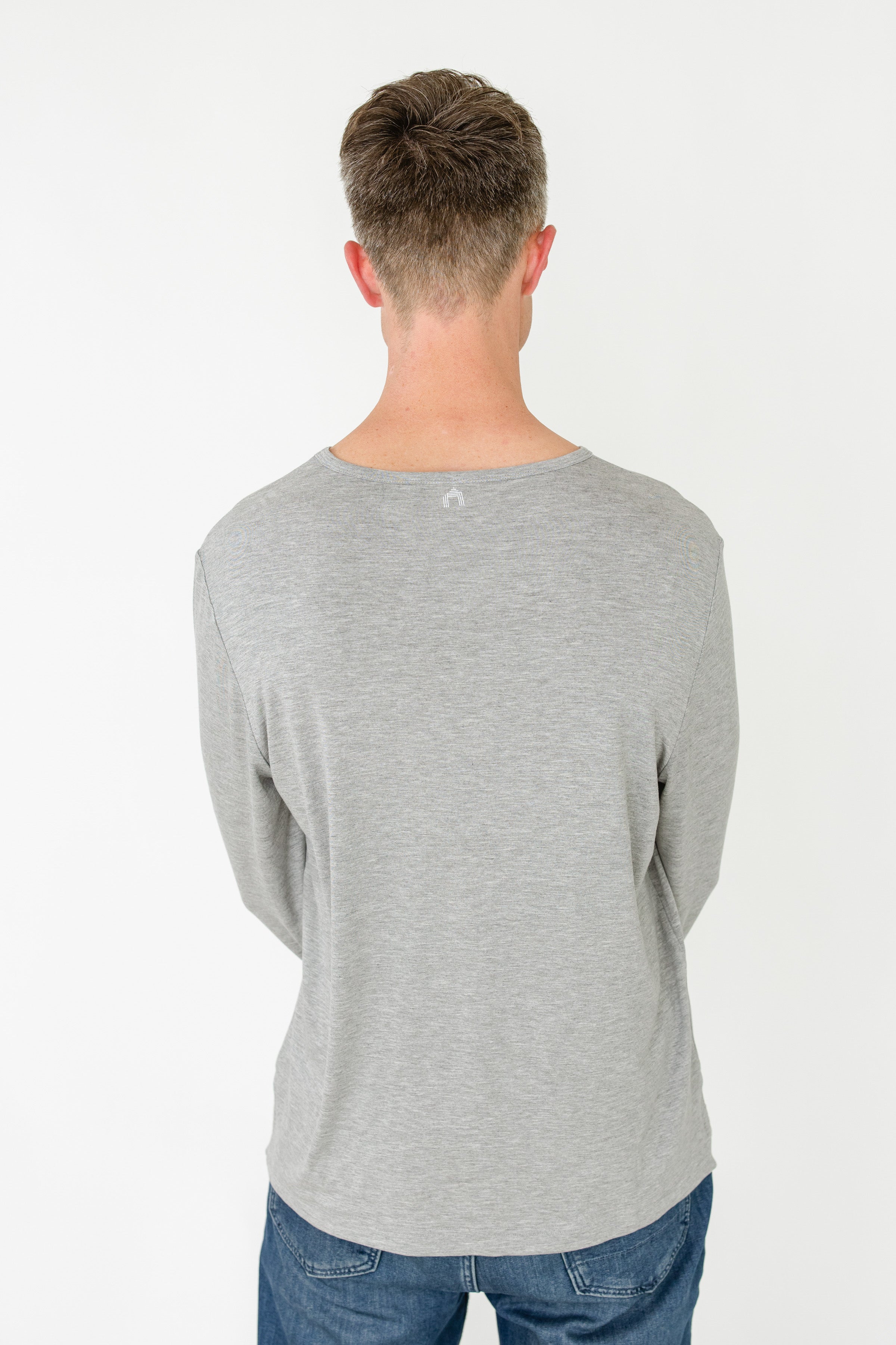 Person wearing a gray long-sleeve shirt and blue jeans on a white background