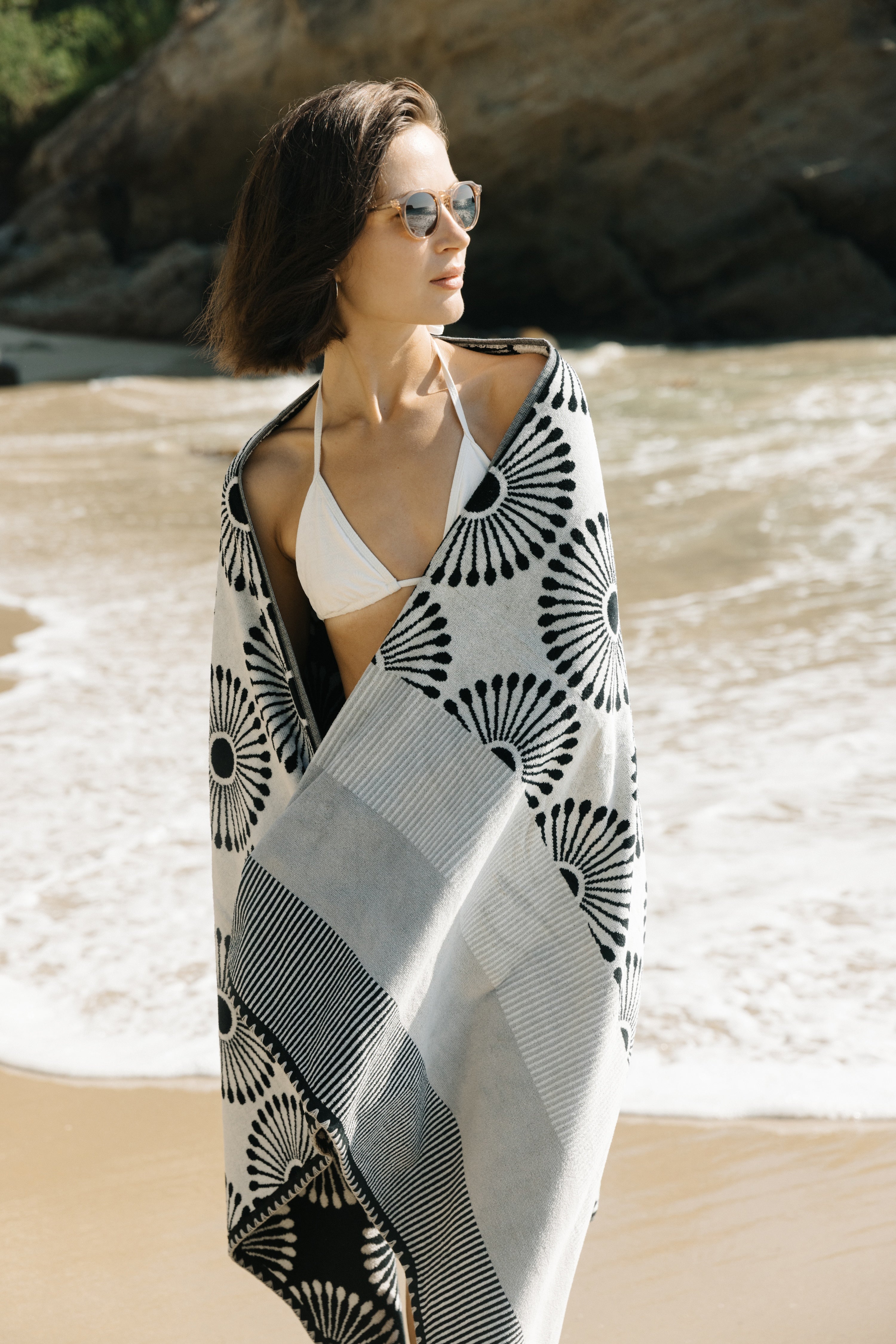 Woman on a beach wearing a black and white patterned cover-up and sunglasses.