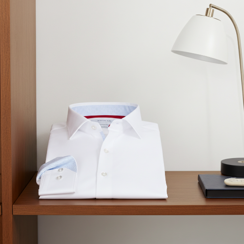 Folded white dress shirt on a wooden shelf with a lamp in the background
