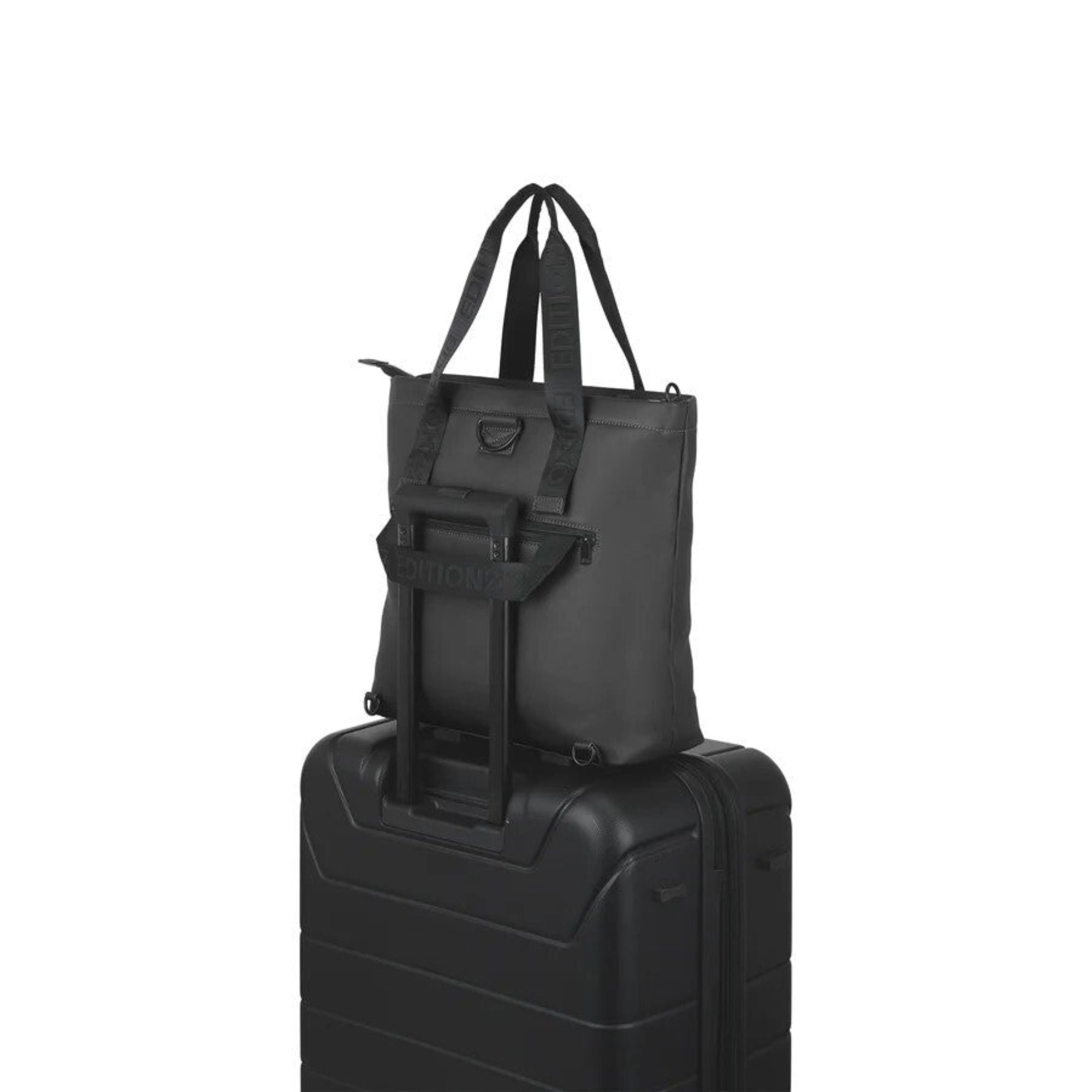 Black tote bag with shoulder strap on top of a black suitcase on a white background