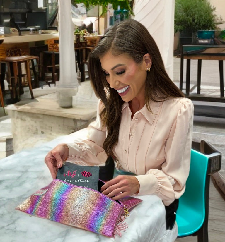 Woman sitting outdoors holding a colorful pouch and a makeup bag with text.