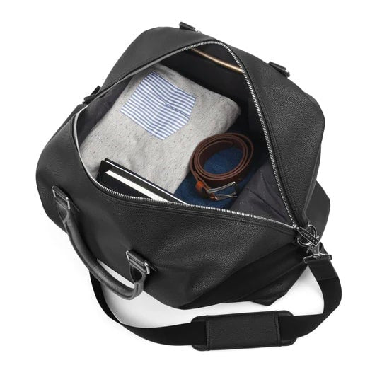 Black duffel bag with items including a striped shirt, belt, and phone on a white background