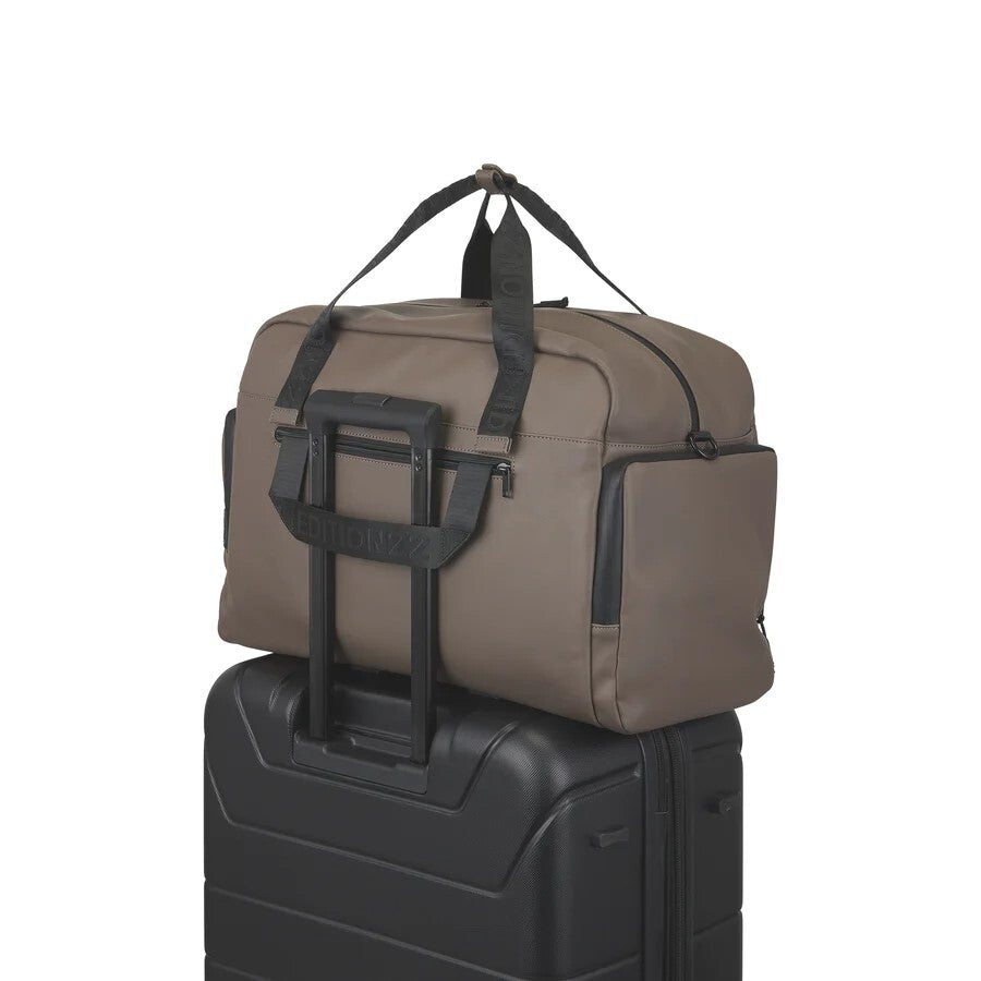 Brown duffel bag with black straps on top of a black suitcase against a white background
