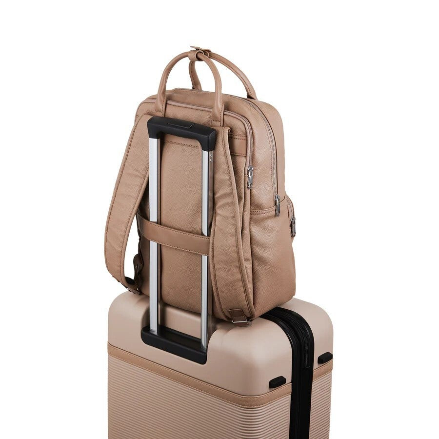 Beige backpack on top of a beige suitcase with a white background