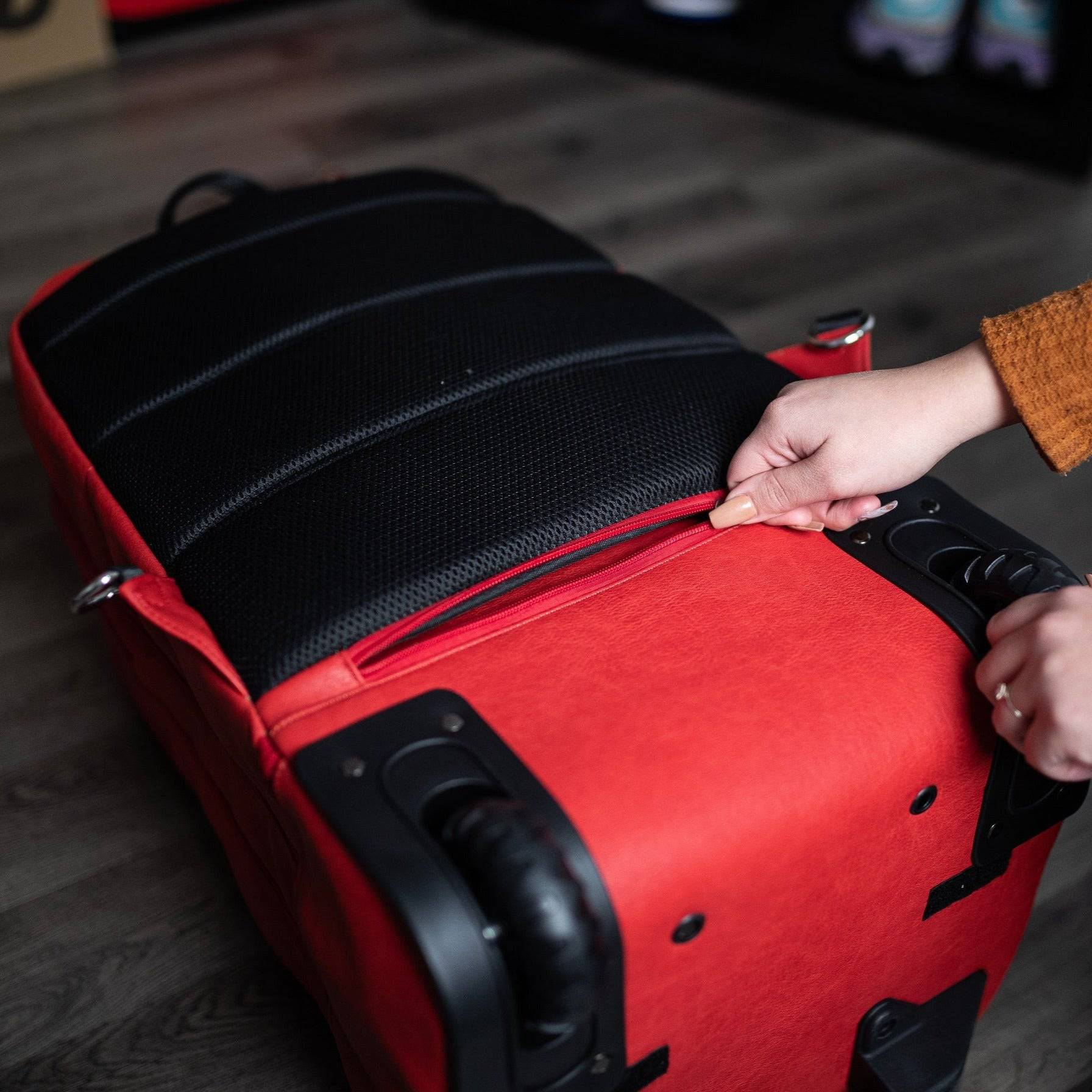 Red suitcase with a person adjusting the handle on a wooden floor.