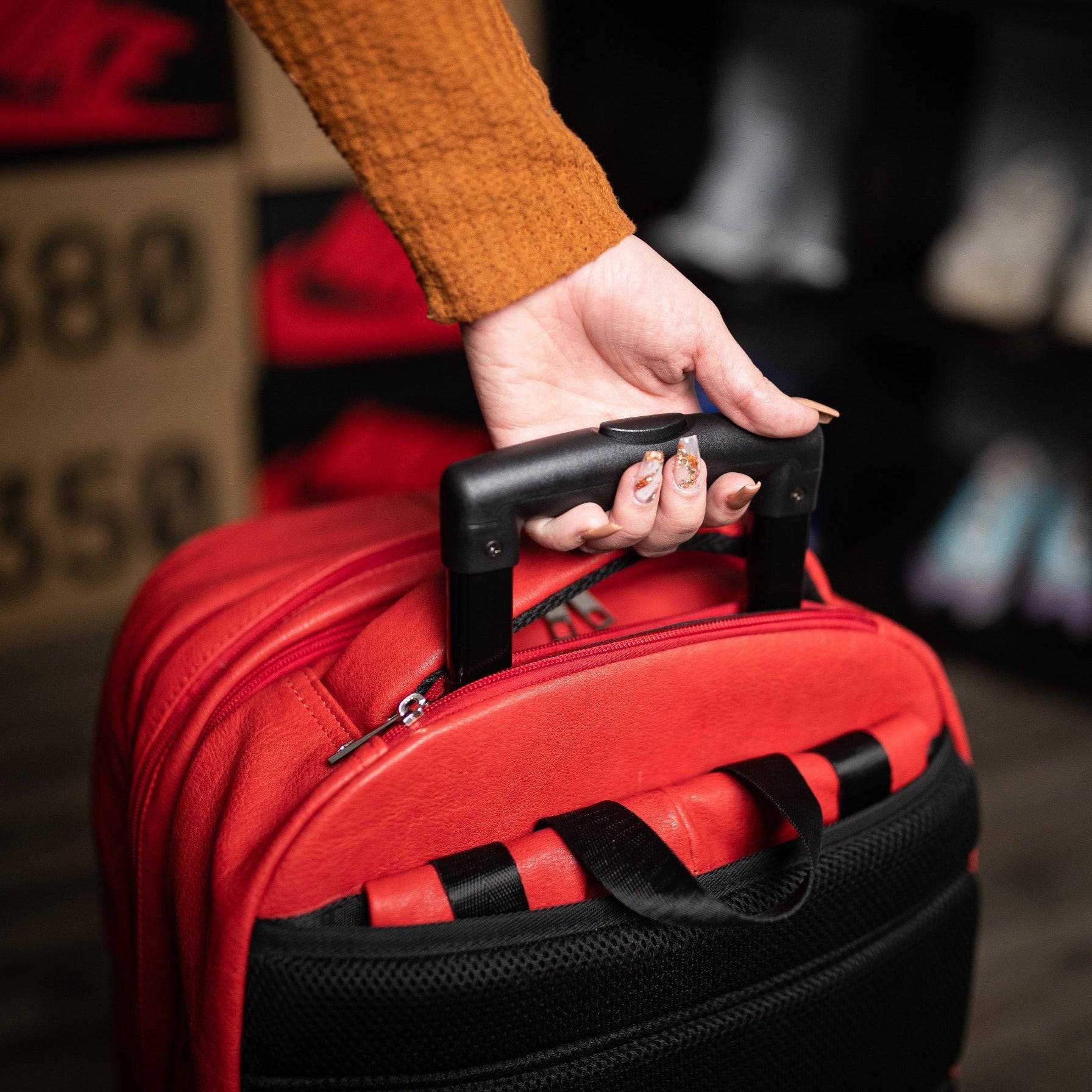 Hand holding a red suitcase with a blurred background