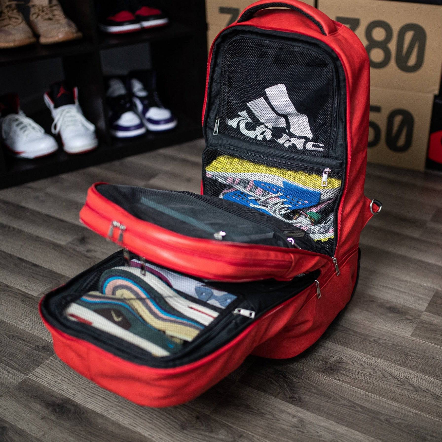 Red backpack with organized compartments on a wooden floor, with shoes in the background.