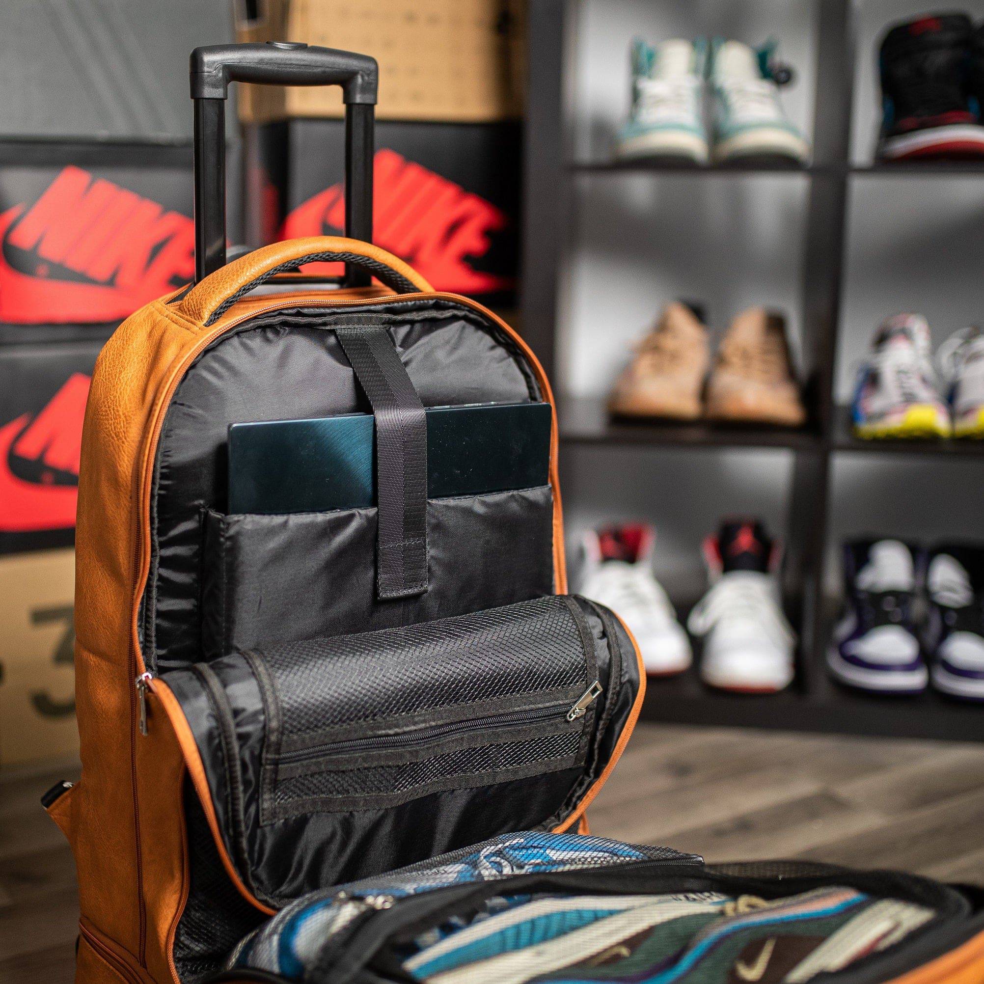Brown backpack with open compartment showing organized items, with a shoe rack in the background.
