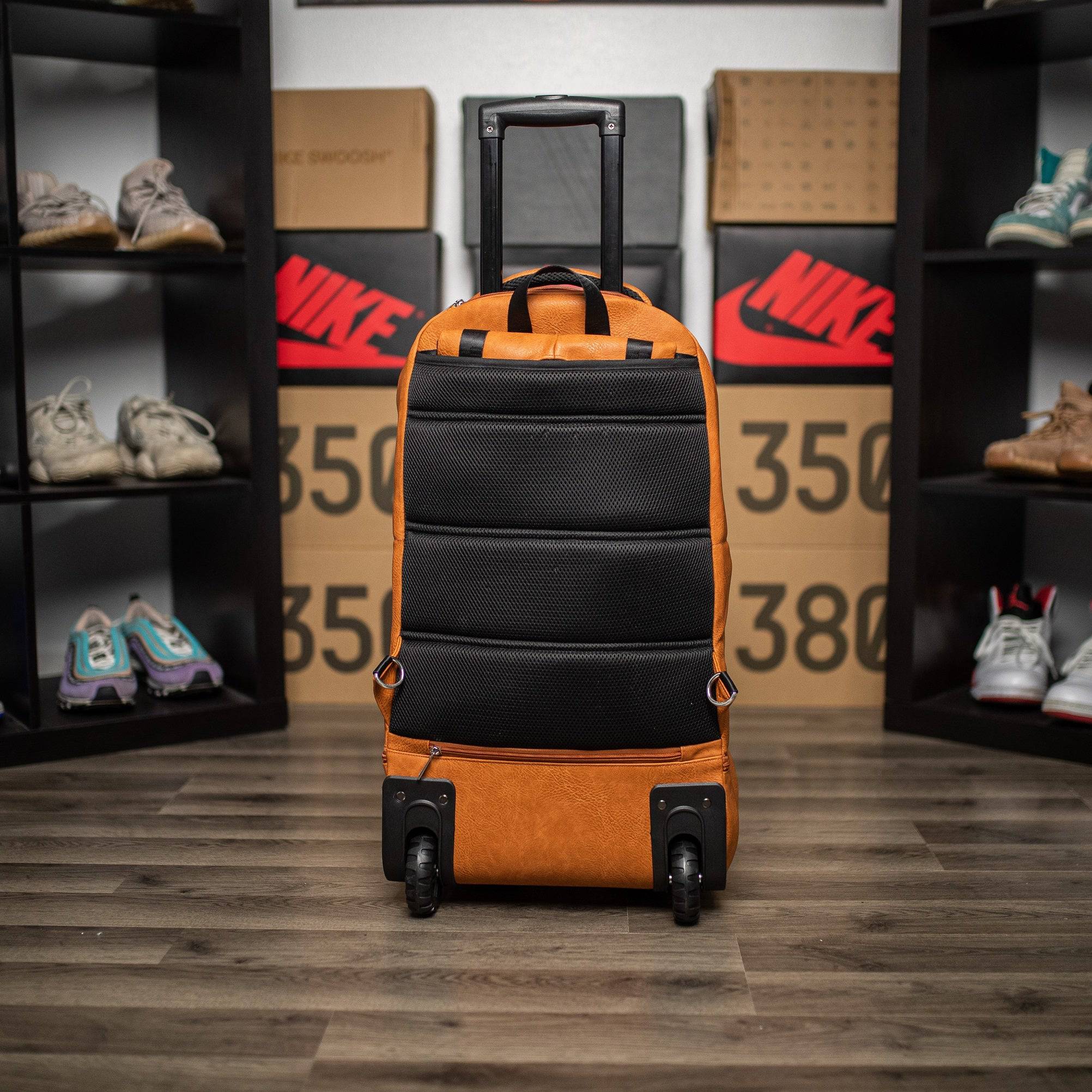 Orange and black suitcase with wheels on a wooden floor with shelves displaying shoes and boxes in the background.