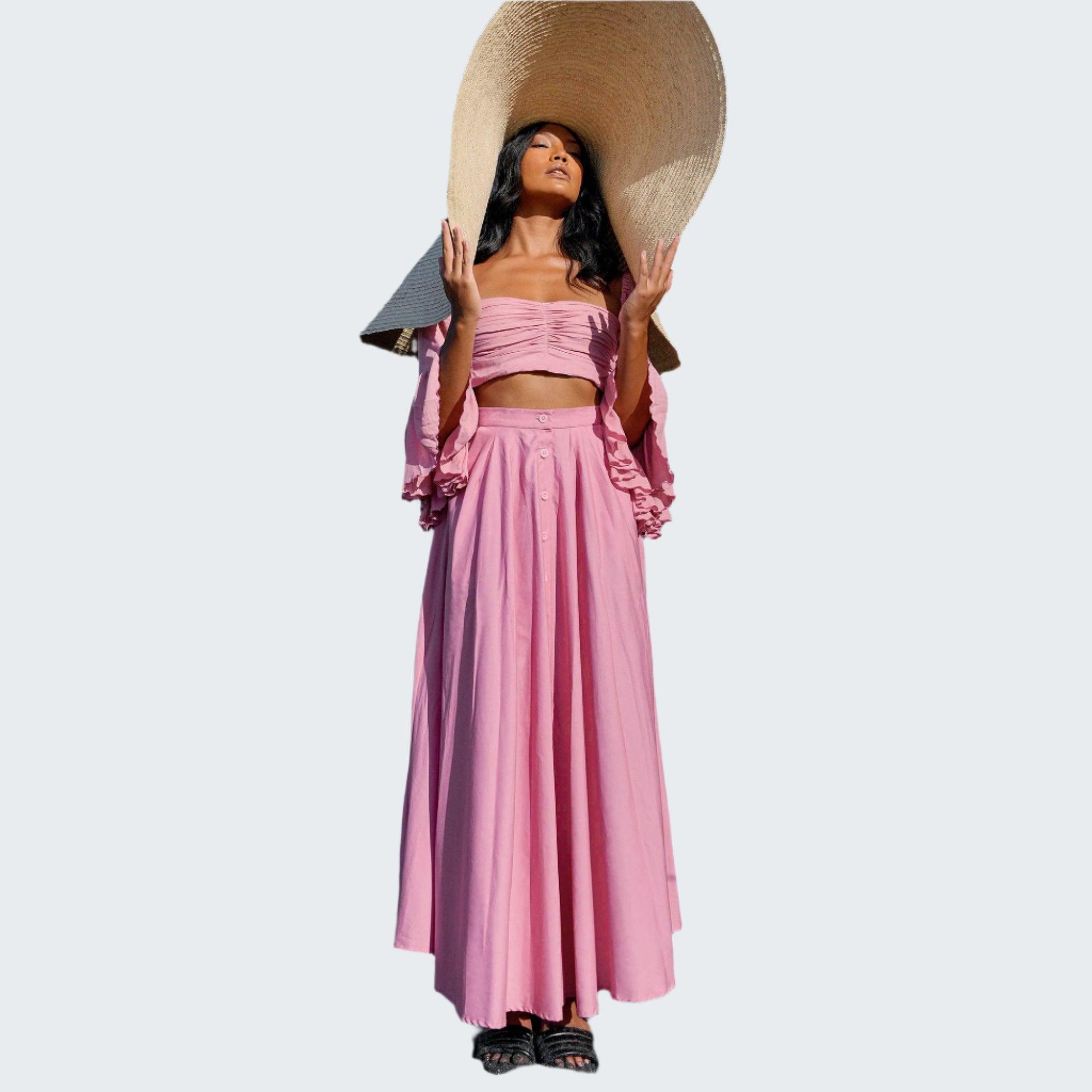 Woman in a pink outfit with a wide-brimmed hat standing in front of green plants.