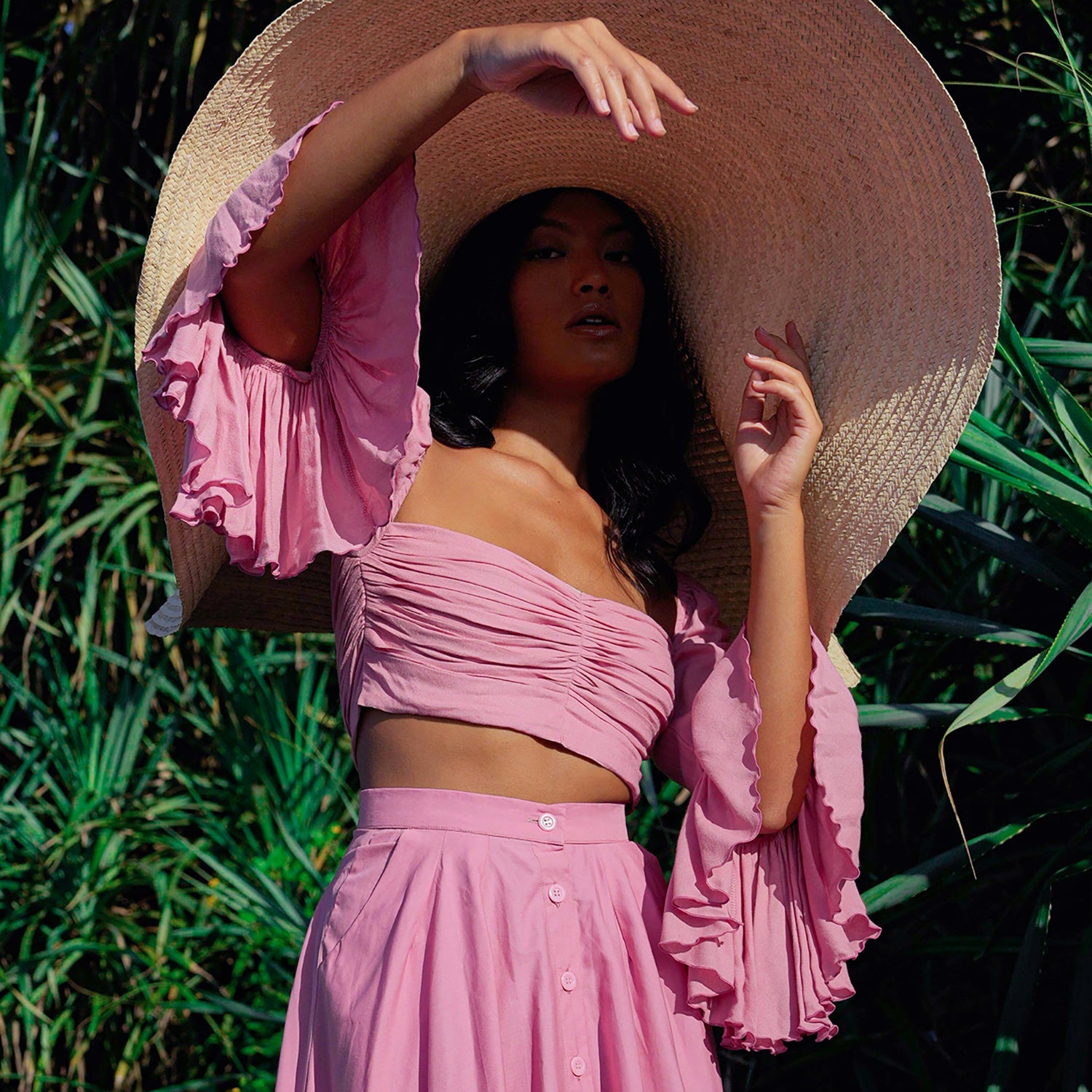 Woman in a pink dress and large straw hat standing in a natural setting