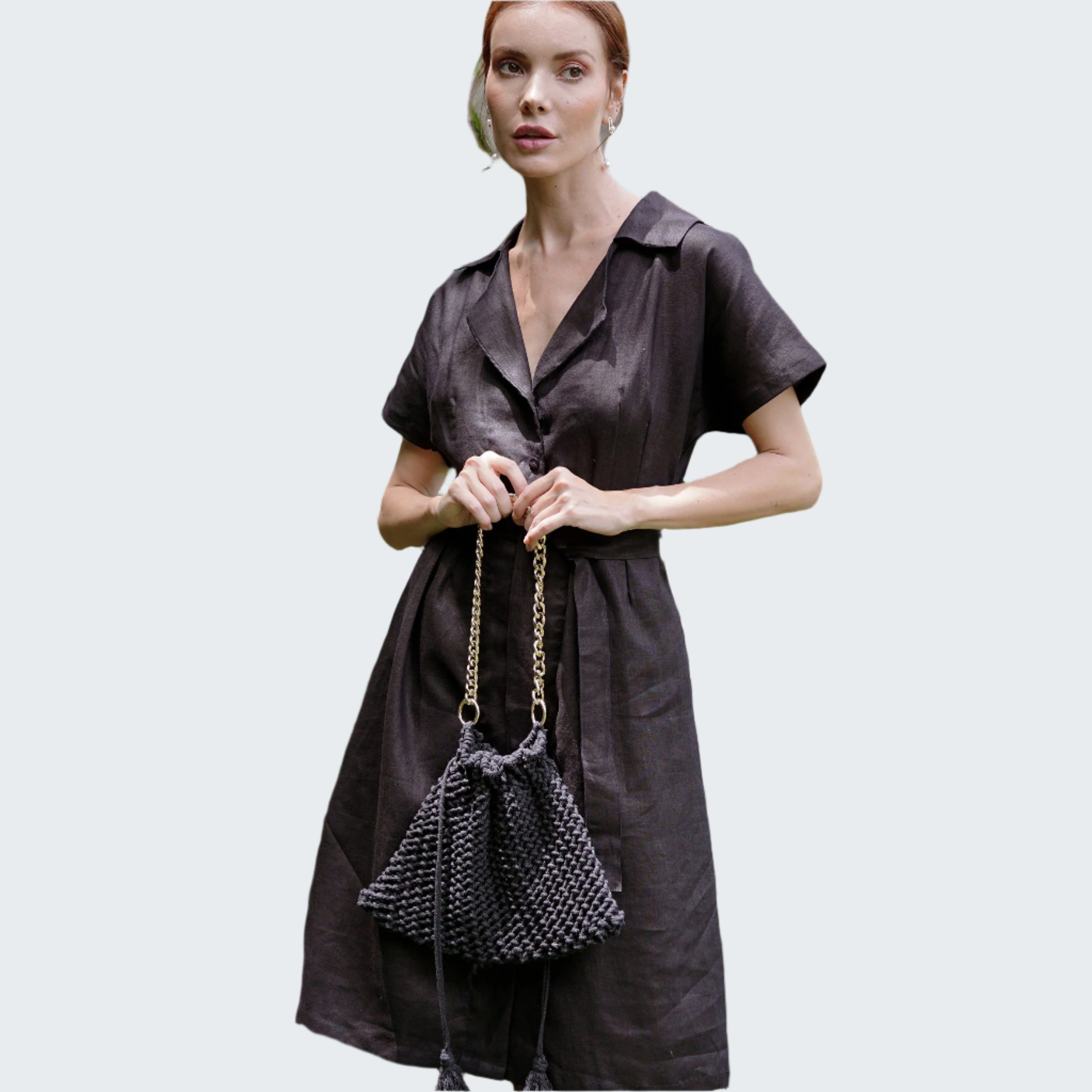 Woman holding a black handbag in front of green foliage