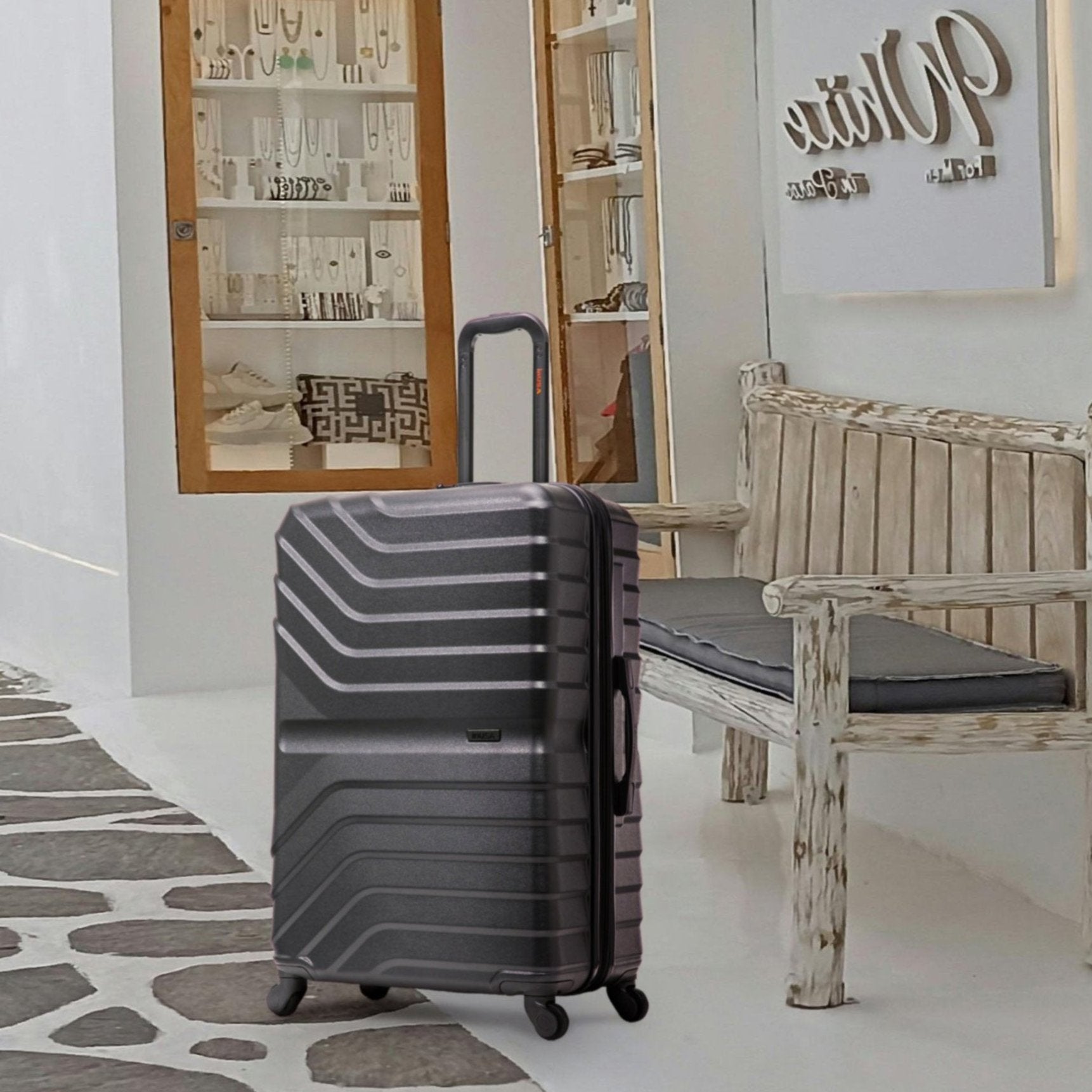 Black suitcase on a stone-patterned floor with a wooden bench and decorative items in the background.