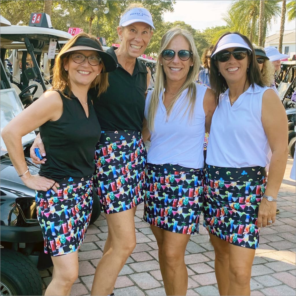Four people posing together at a golf event, wearing colorful skirts.