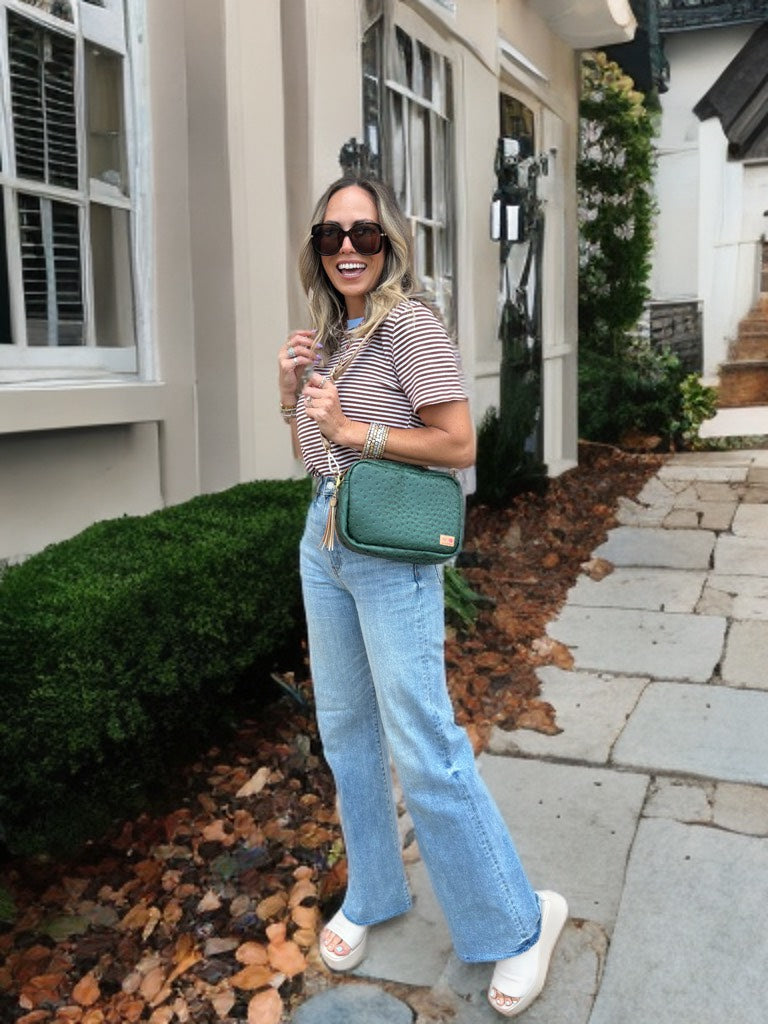 Woman in striped shirt and jeans holding a green bag on a sidewalk.