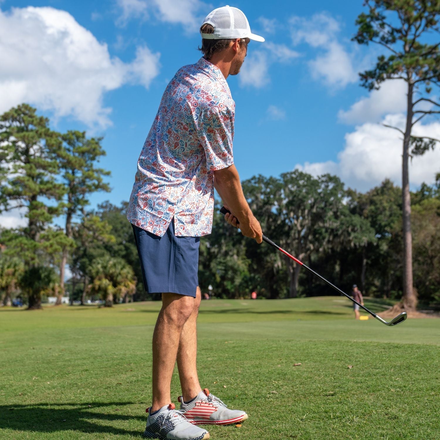 Man playing golf on a green course with trees and blue sky in the background