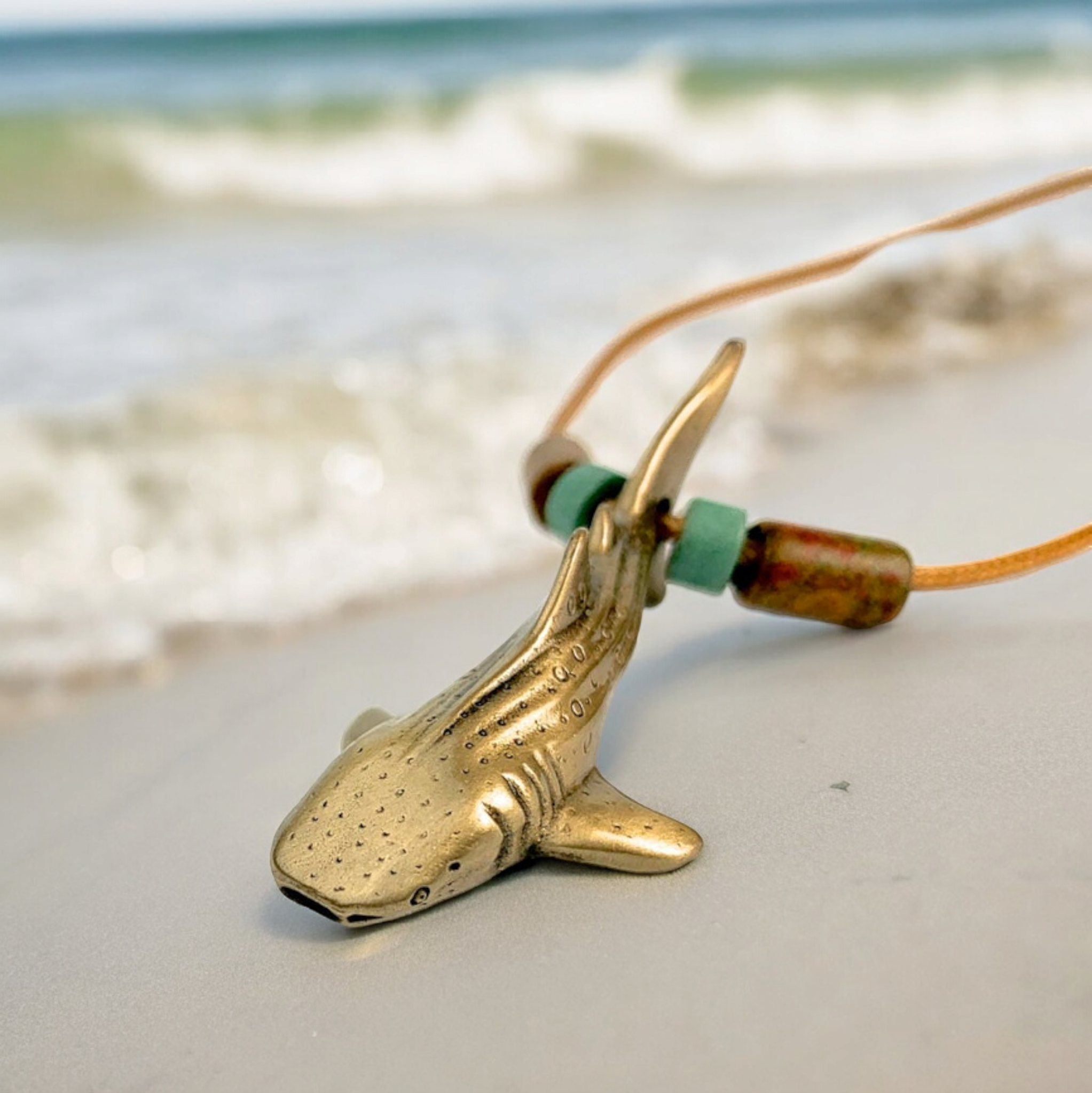 Brass shark pendant on a cord with a beach background