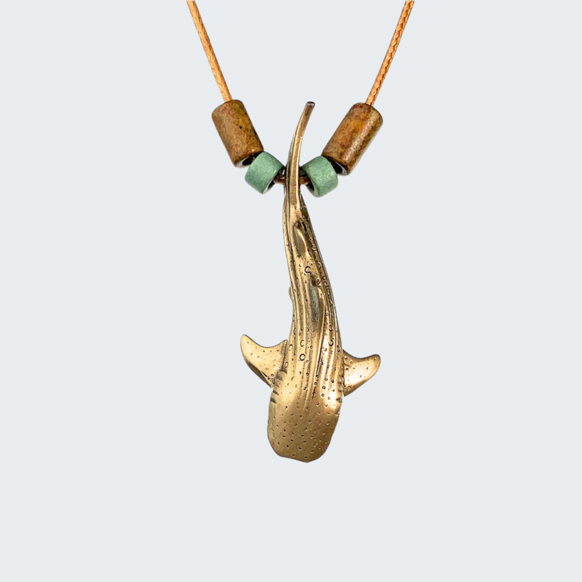 Brass shark pendant necklace with wooden and green beads on a light gray background