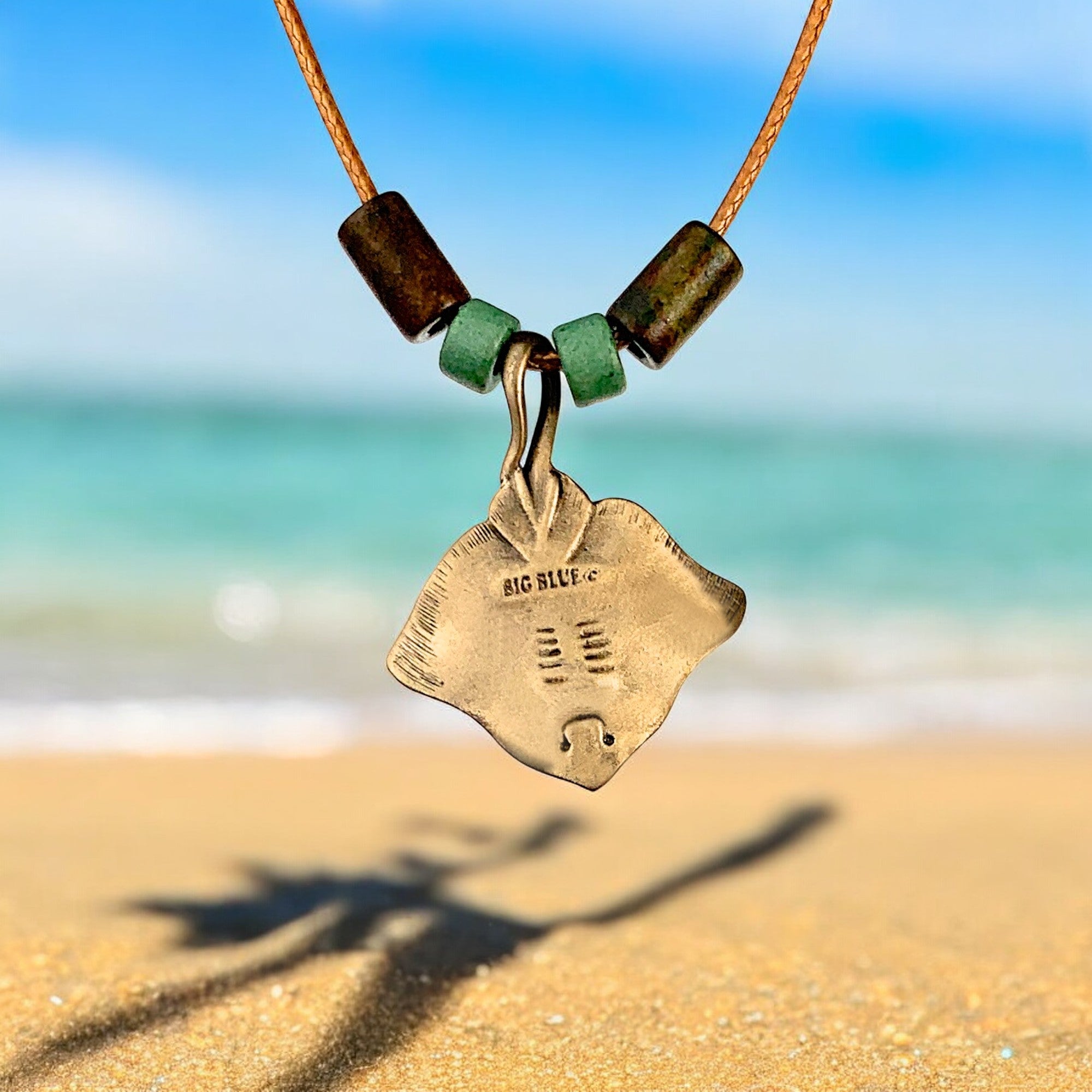 Necklace with a pendant shaped like a stingray on a sandy beach with ocean in the background
