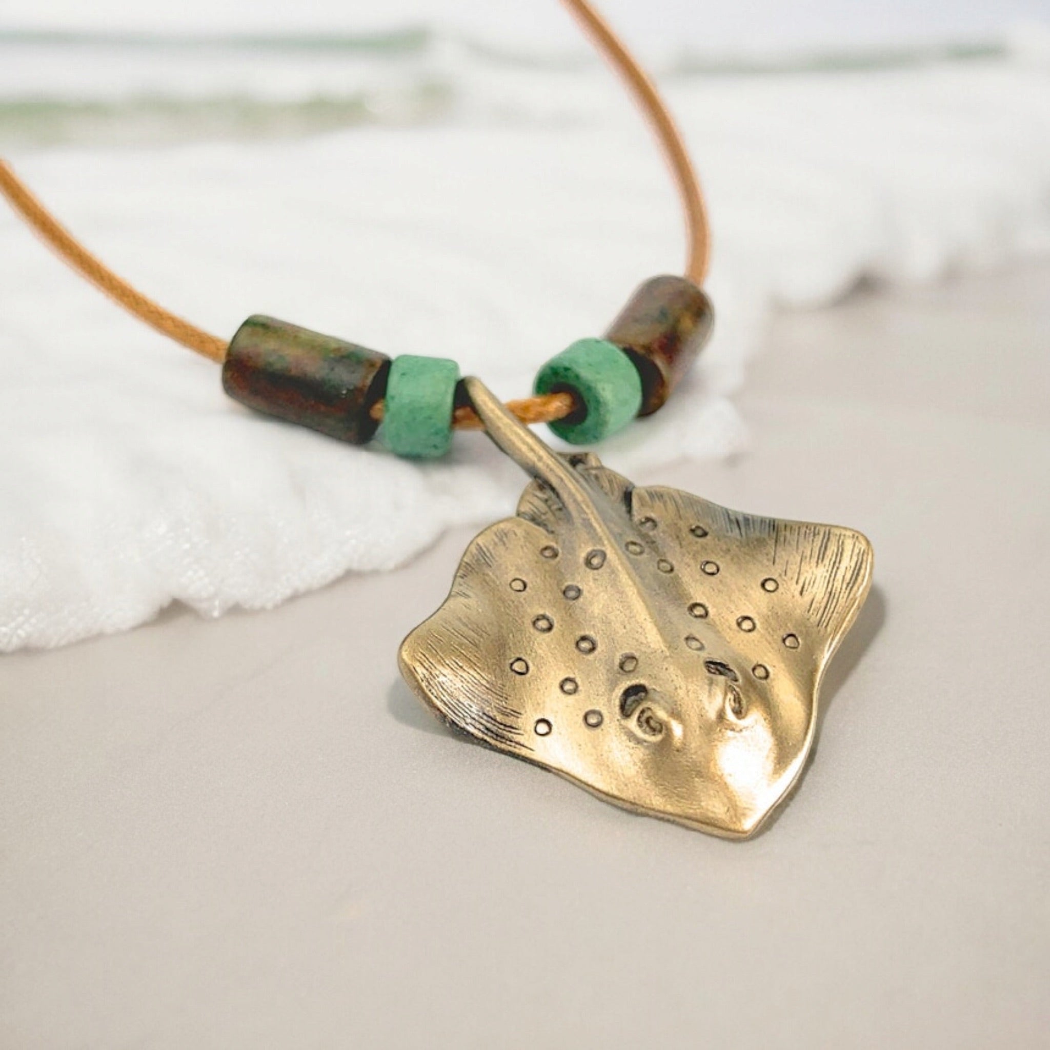 Brass stingray pendant on a cord with green beads against a white background